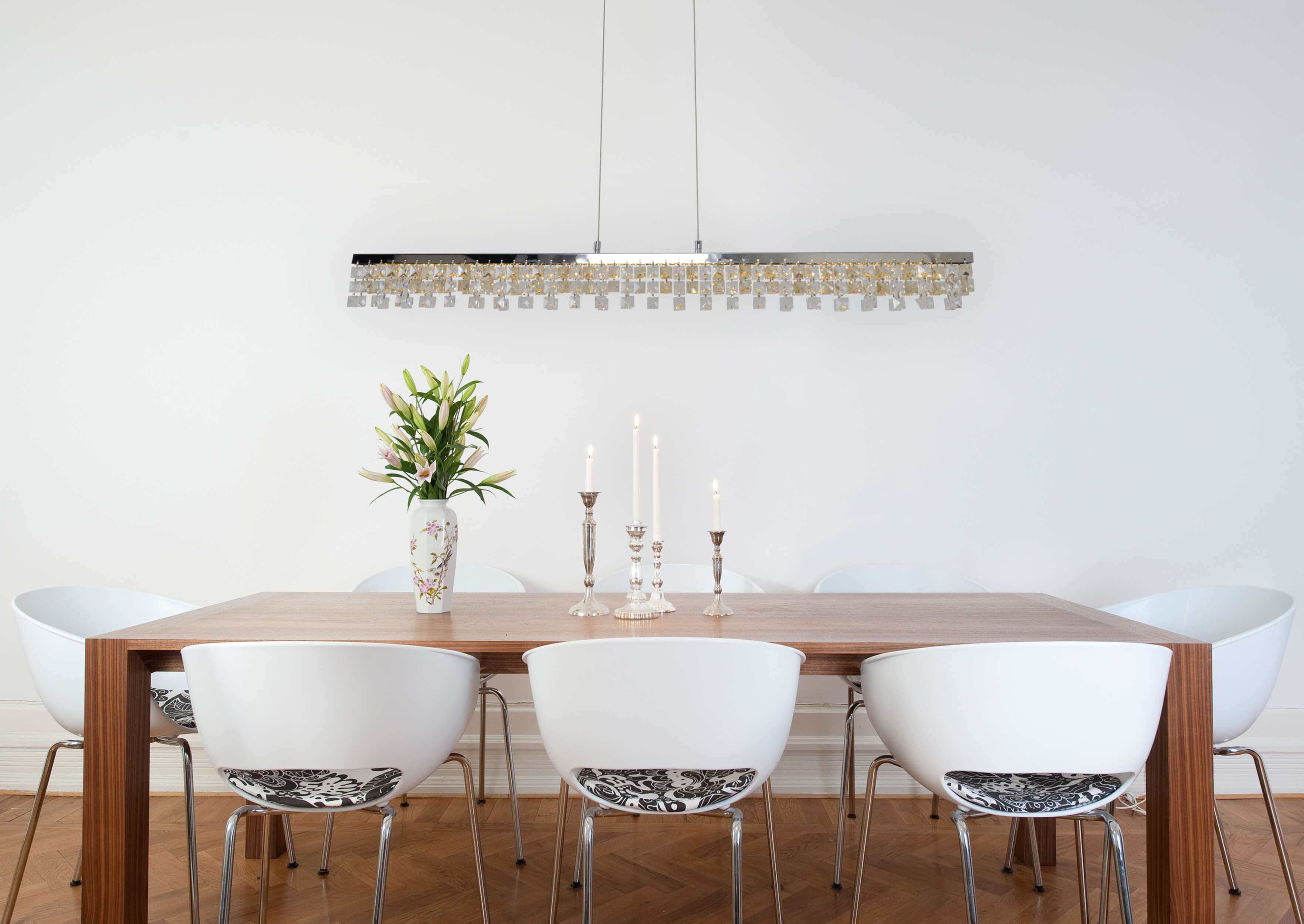 Esszimmer mit einem langen Holztisch, weißen Stühlen und einem Kronleuchter mit Kristallakzenten.