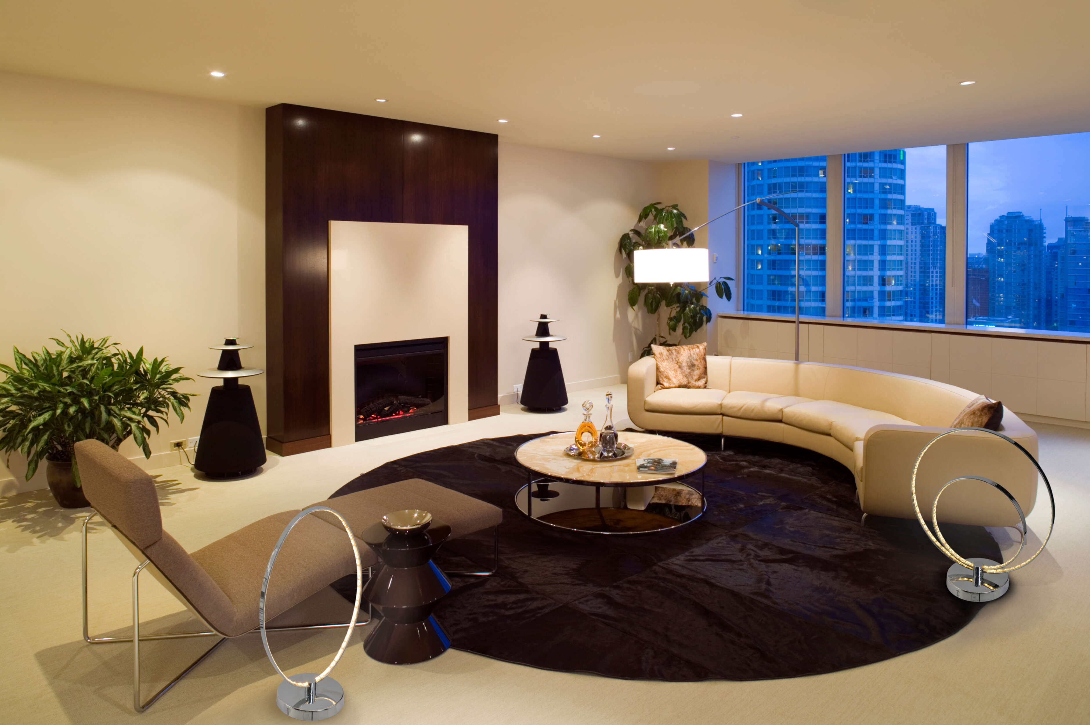 Modernes Wohnzimmer mit Kamin, geschwungenem Sofa und mehreren ringförmigen Lampen.