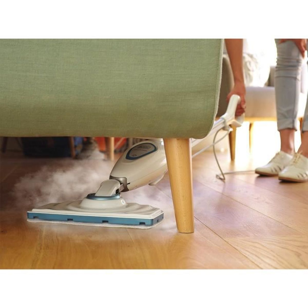 Odkurzacz parowy czyszczący drewnianą podłogę pod sofą. Osoba widoczna w tle.
