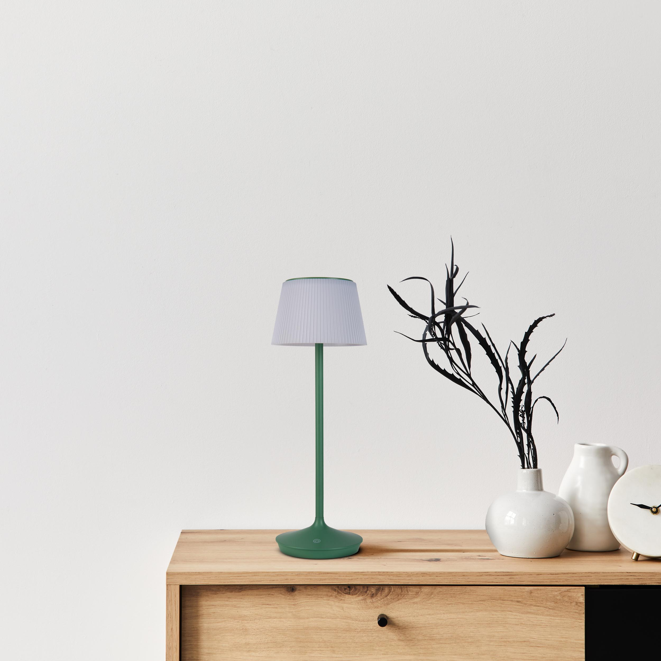 Grüne Lampe auf Holzoberfläche mit weißem Wandhintergrund.