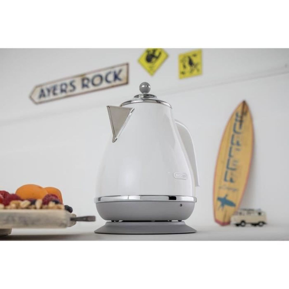 White and gray electric kettle on a gray base. Other items: fruit tray, surfboard, and Ayers Rock sign.