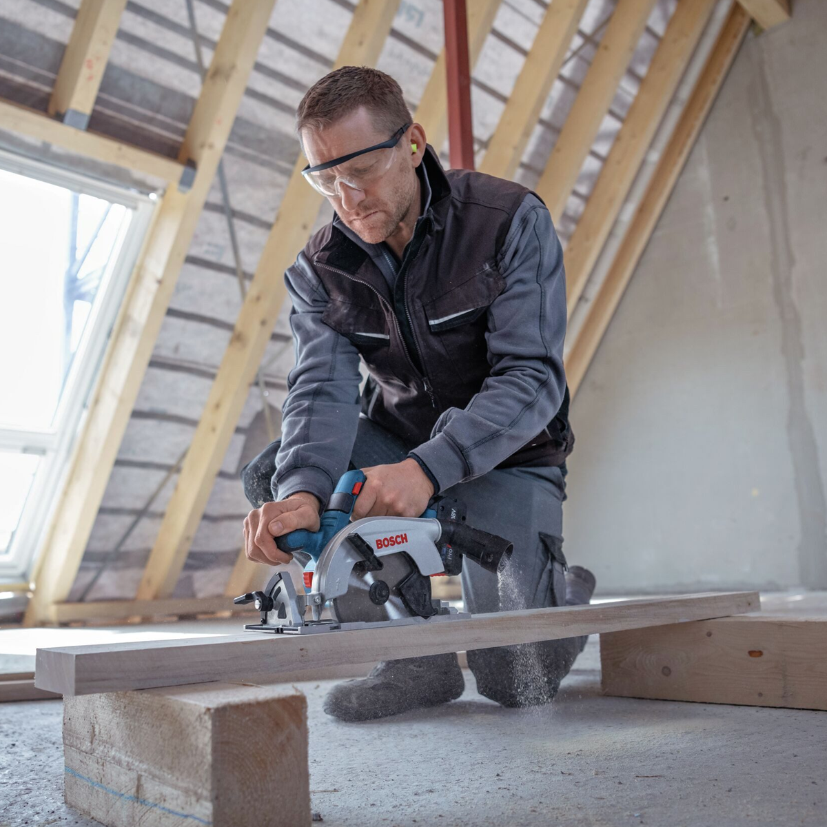 Ein Mann benutzt eine Kreissäge, um Holz zu schneiden. Er trägt Schutzbrille und Ohrenstöpsel.