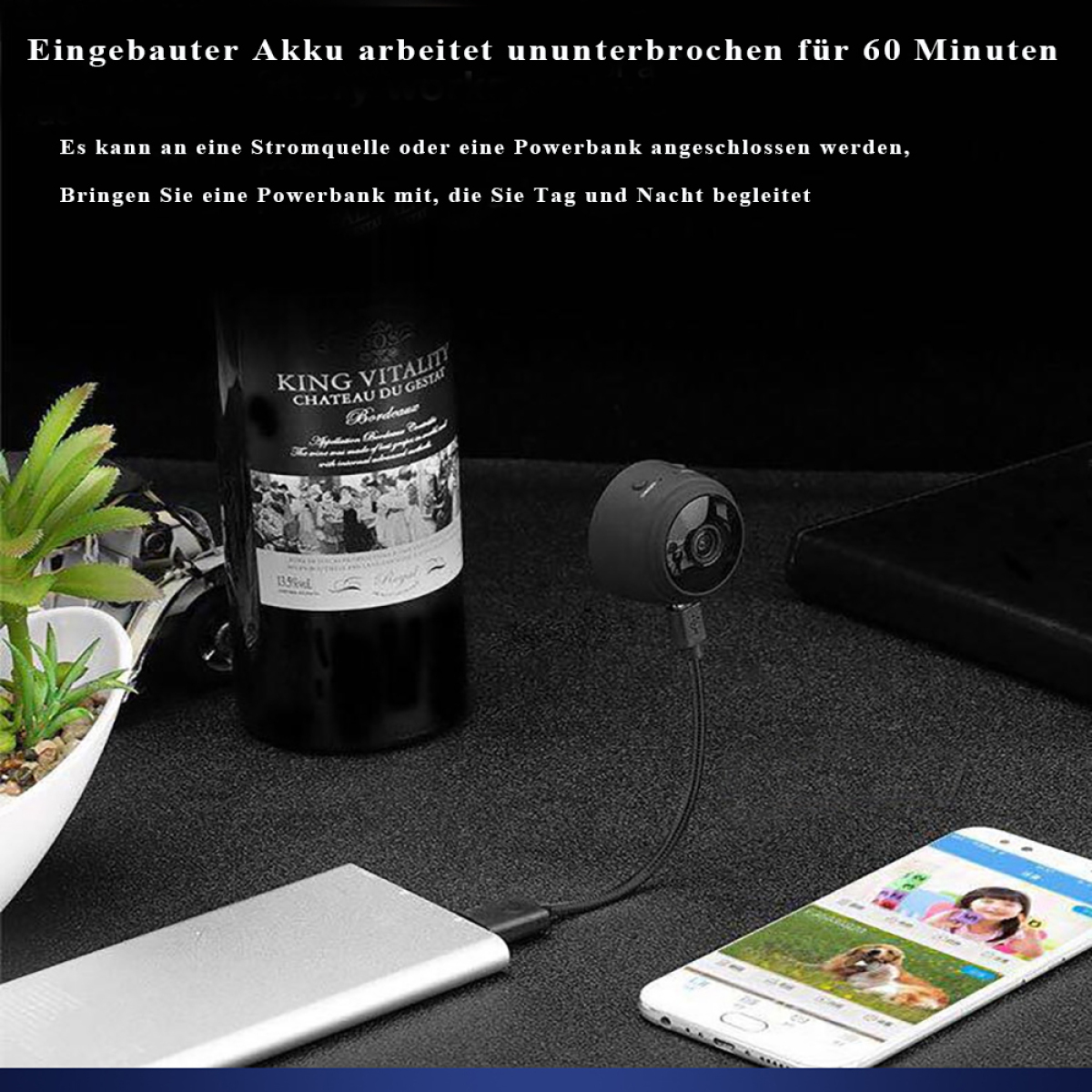 Kleine schwarze Überwachungskamera mit Telefon verbunden. Weinflasche und Topfpflanze auf dem Schreibtisch.
