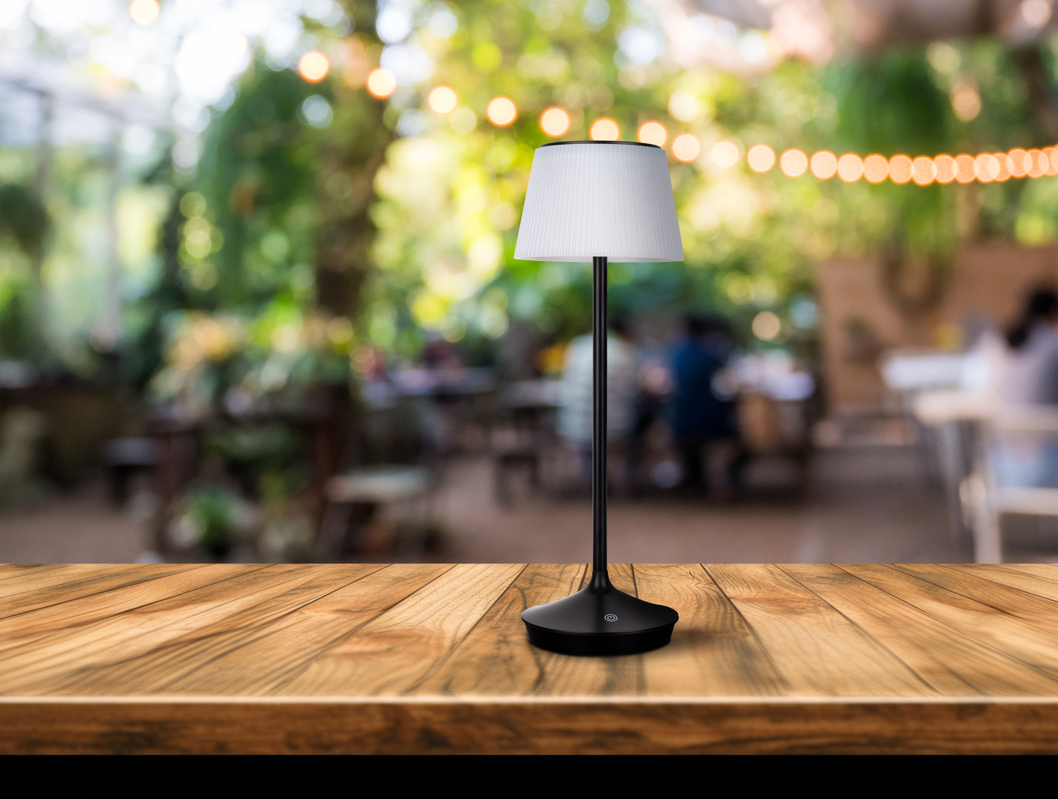 Tischlampe auf Holztisch. Weißer Lampenschirm, schwarzer Stiel, schwarzer Sockel. Verschwommener Hintergrund eines Restaurants.