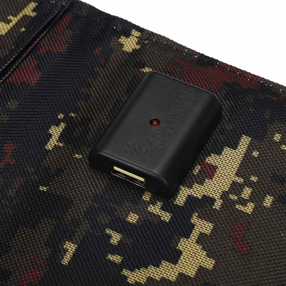Schwarzes USB-Ladegerät mit USB-Anschluss und rotem Licht auf Camouflage-Oberfläche.