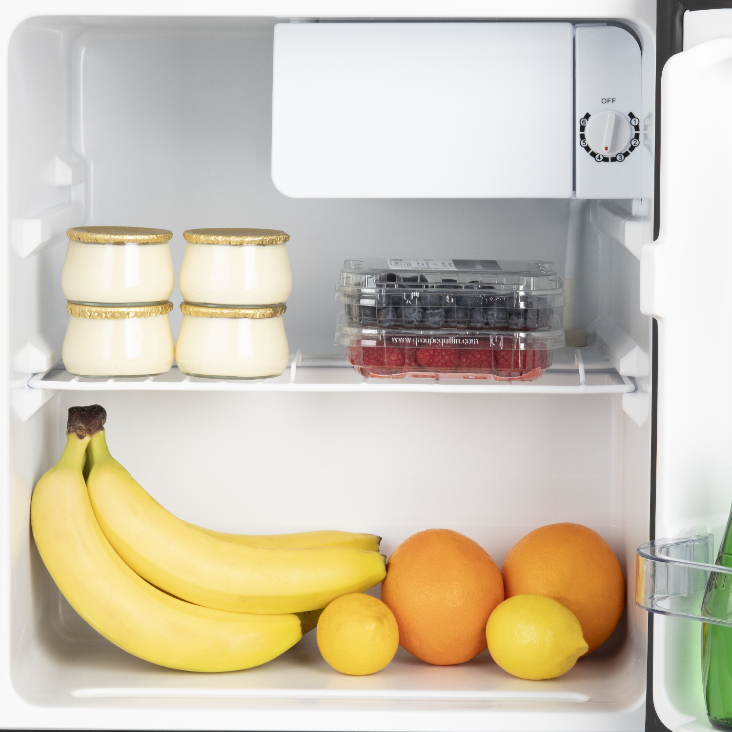 Interno di un mini frigorifero con yogurt, bacche, banane, arance e limoni.