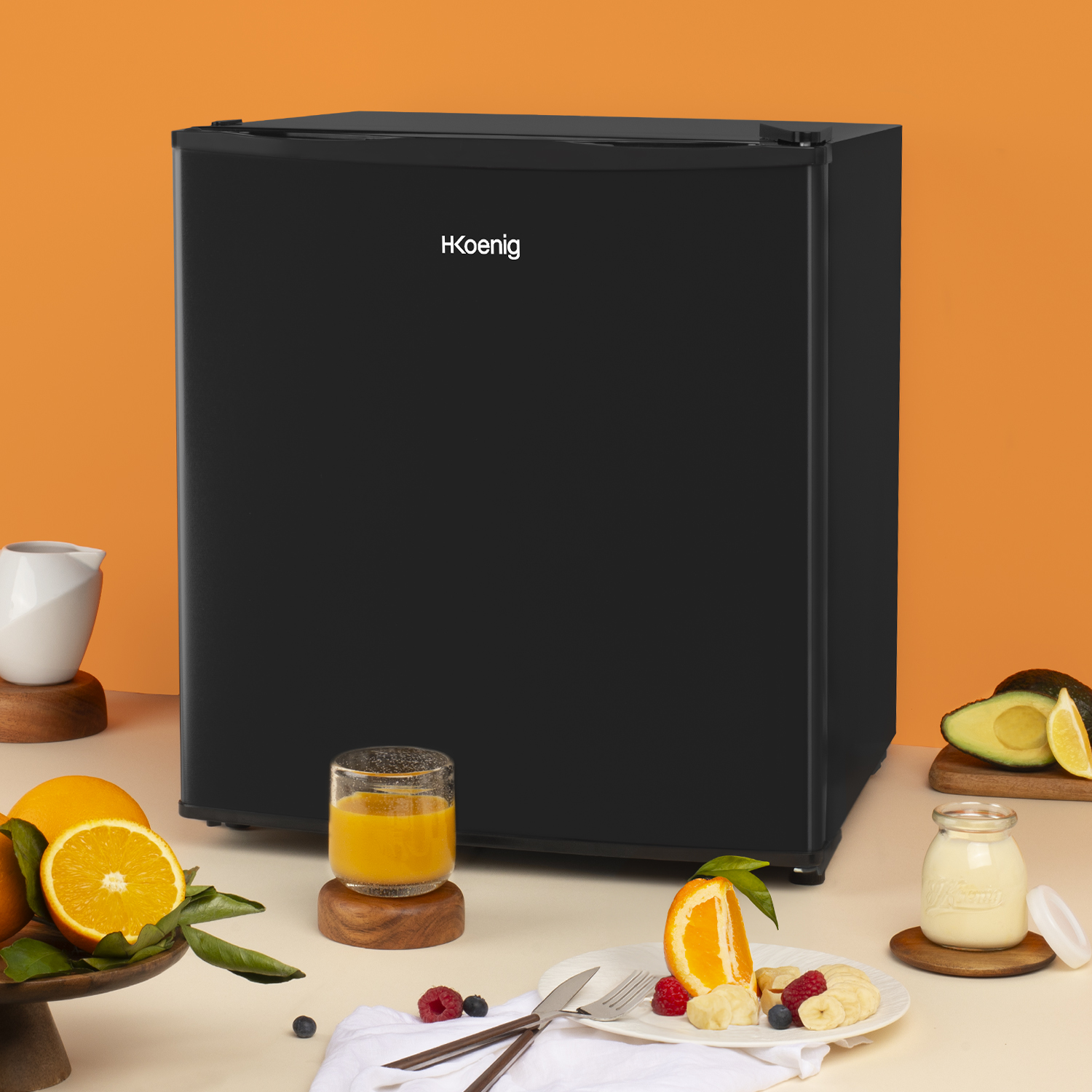 Mini-frigorifero nero su sfondo arancione, circondato da frutta, succo e altri alimenti.