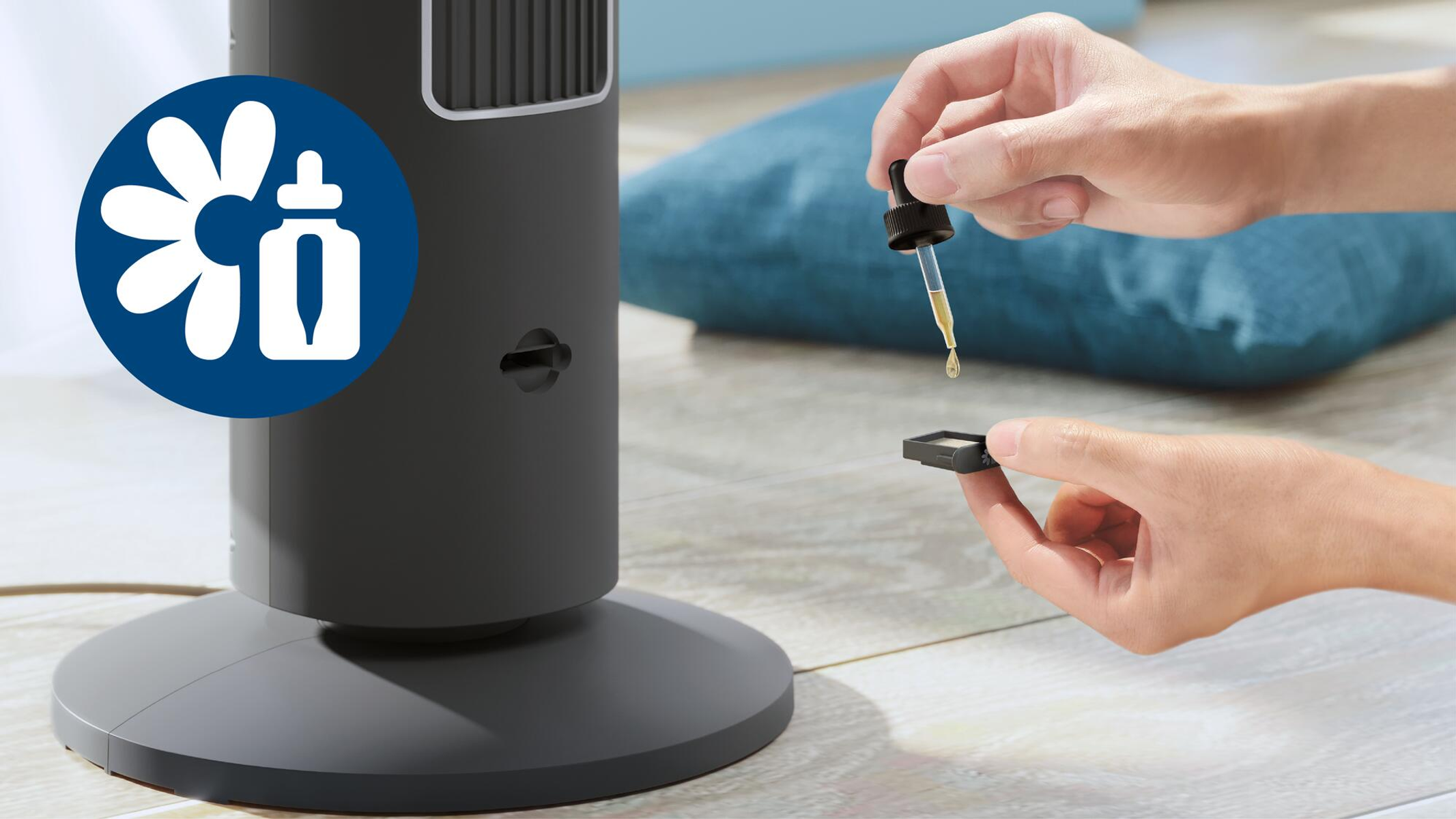 Hände, die Öltropfen in einen schwarzen Diffusor geben. Ein Ventilator im Hintergrund.