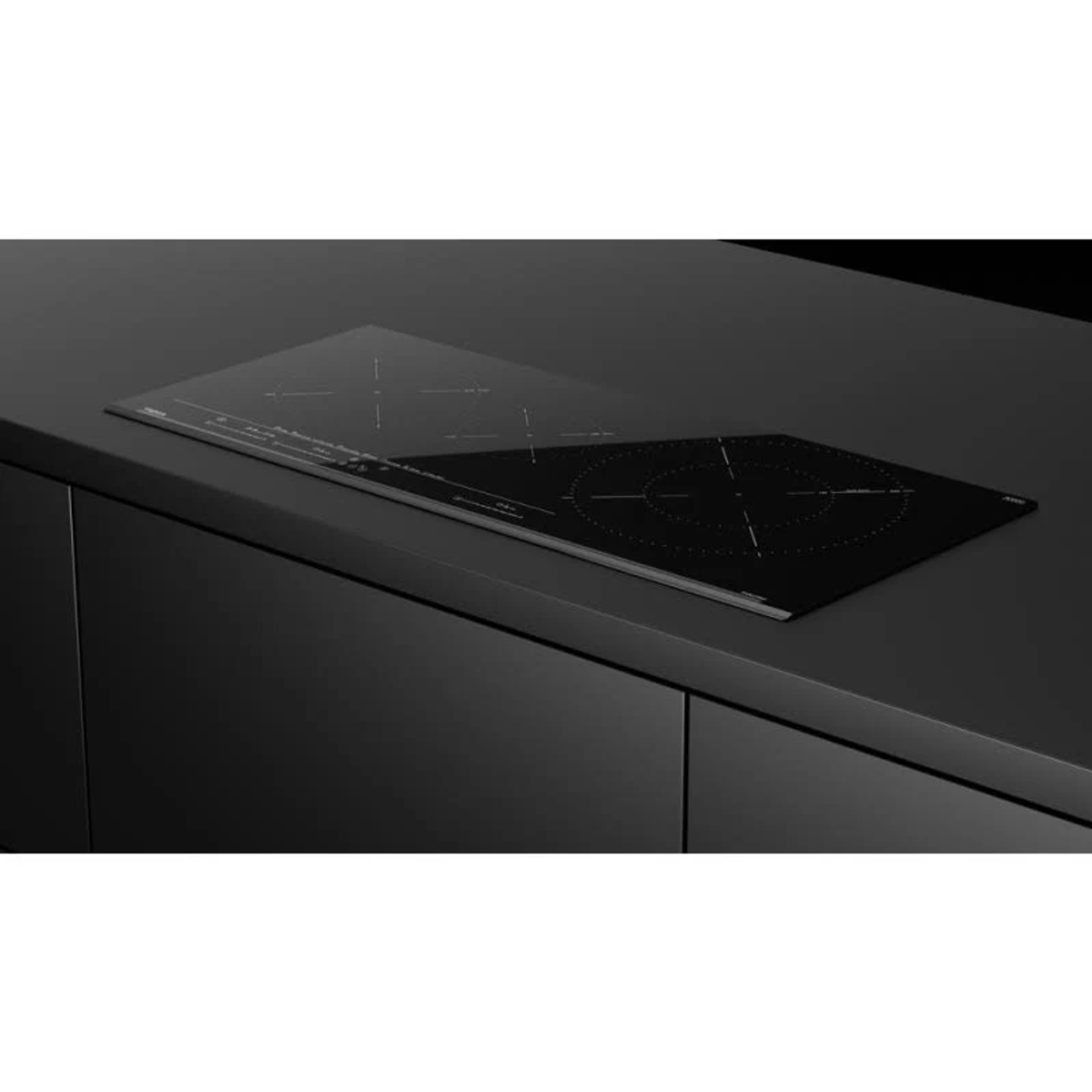 Czarna płyta indukcyjna, zainstalowana na czarnej powierzchni, pokazująca strefy gotowania i panel sterowania.