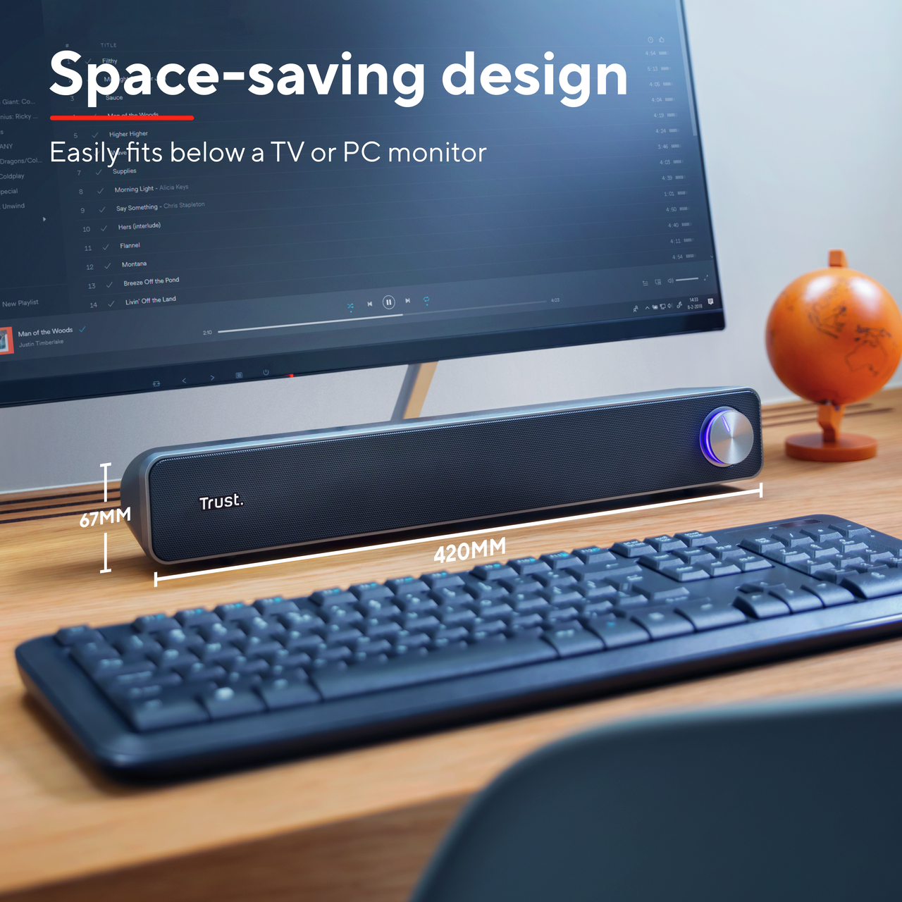 Czarny soundbar z niebieskim światłem na drewnianym biurku, z klawiaturą i monitorem.