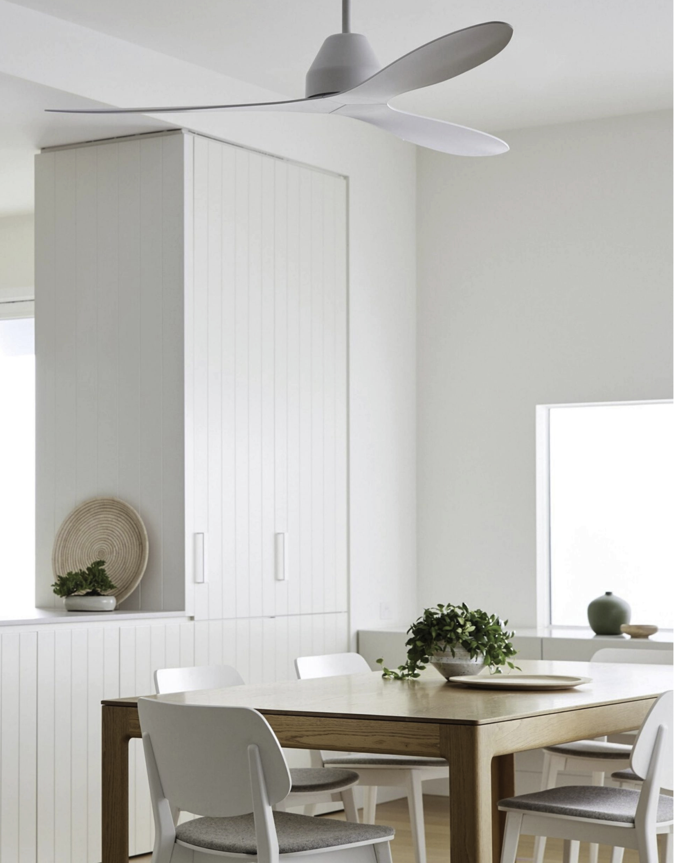 Sala da pranzo bianca con tavolo in legno, sedie e ventilatore a soffitto. Stile minimalista.