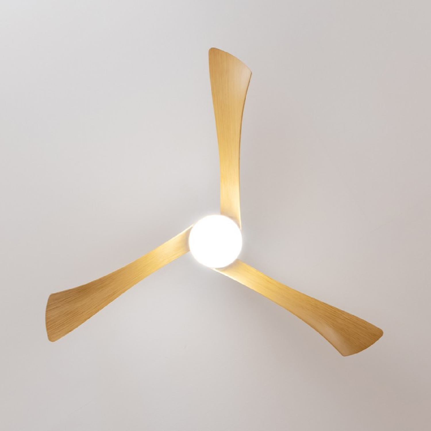 Deckenventilator mit drei gebogenen Holzflügeln und einer zentralen Leuchte, an weißer Decke montiert.