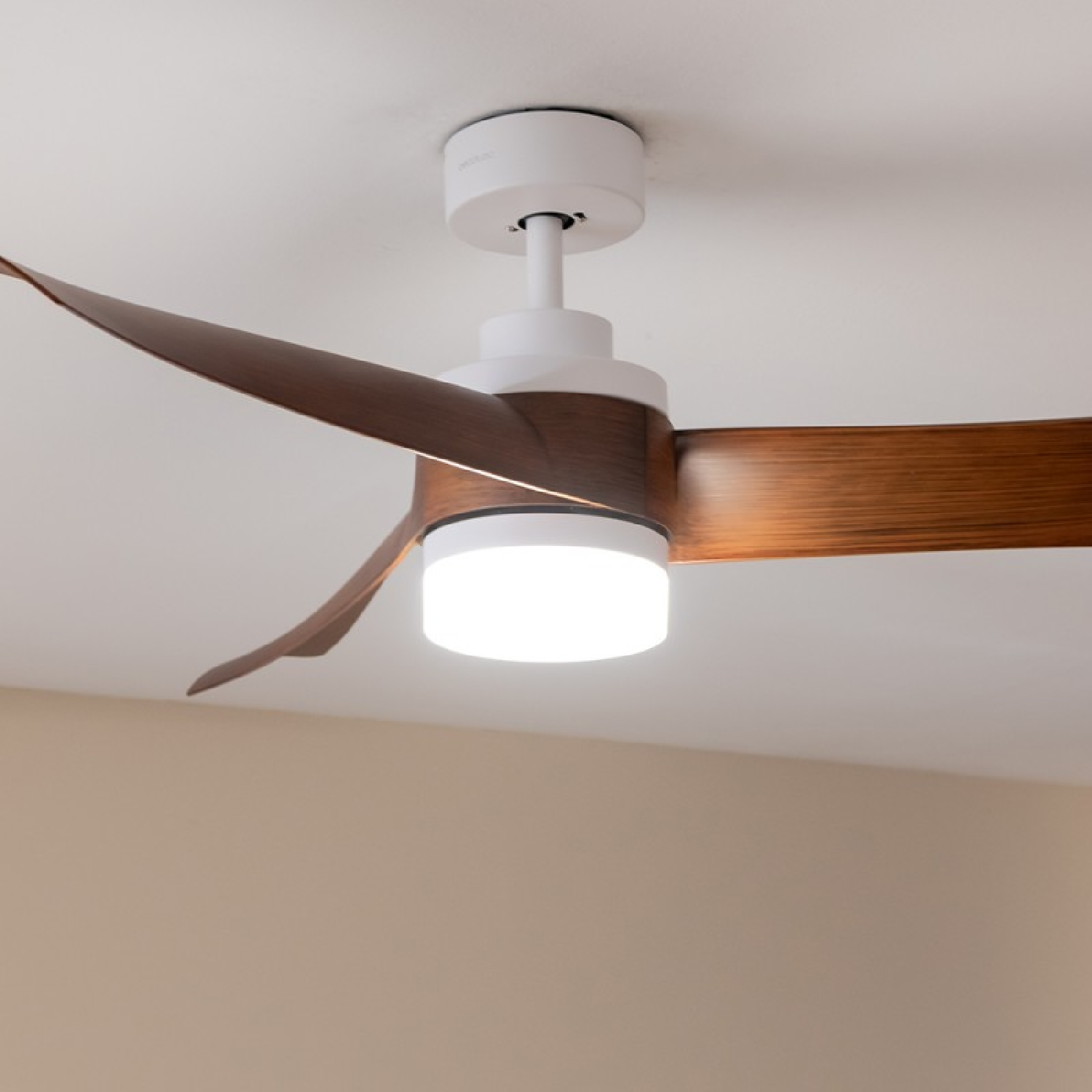 Un ventilatore a soffitto con tre pale marroni e una luce centrale. Il corpo bianco è visibile.