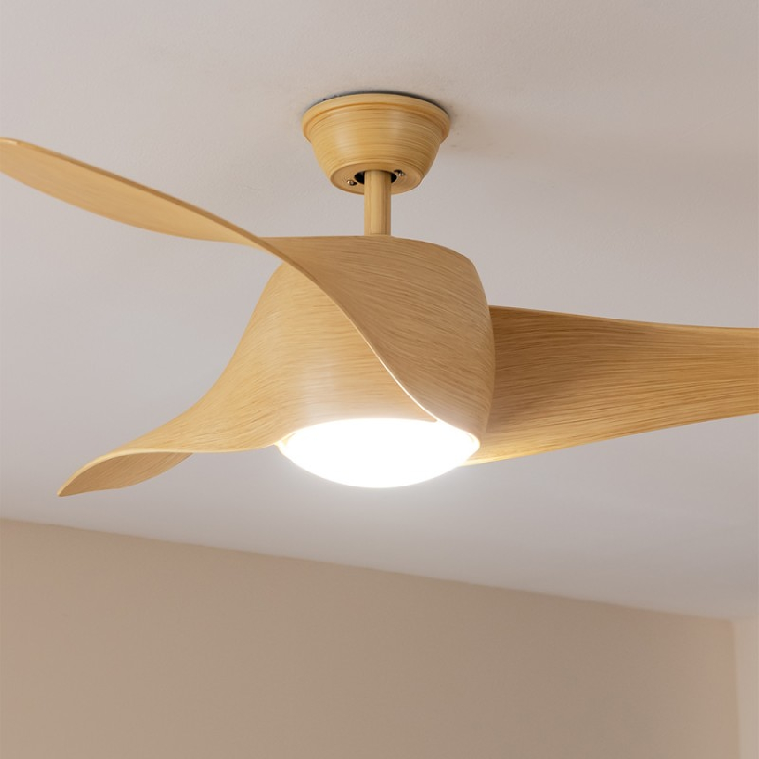 Un ventilatore a soffitto con tre pale in legno chiaro e una luce centrale, con uno sfondo beige chiaro.