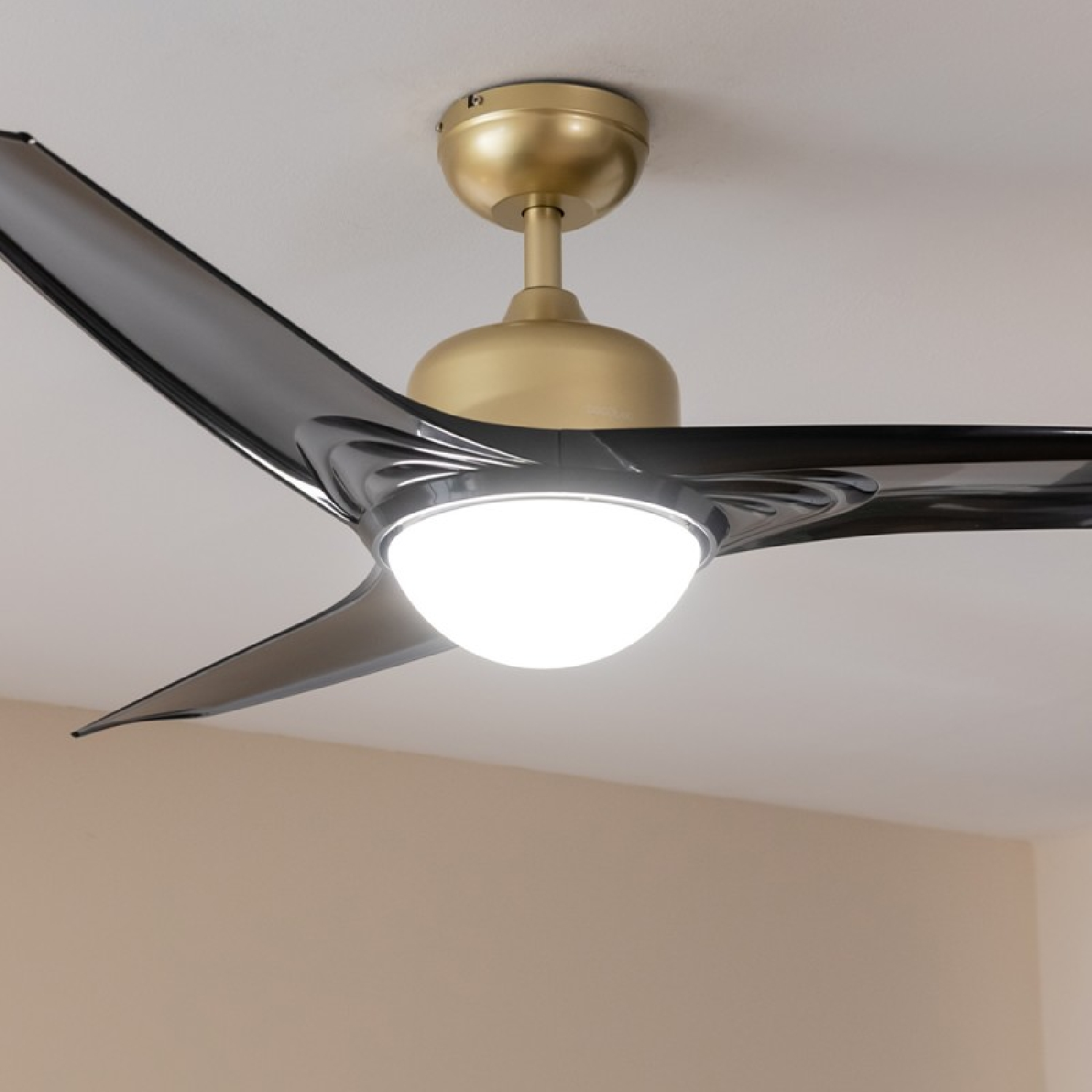 Un ventilatore da soffitto con tre pale nere e una base dorata. Una luce bianca al centro.