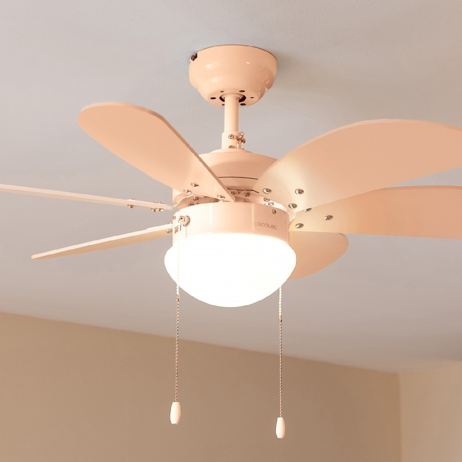 Un ventilador de techo con cinco aspas y una lámpara. Color rosa claro.