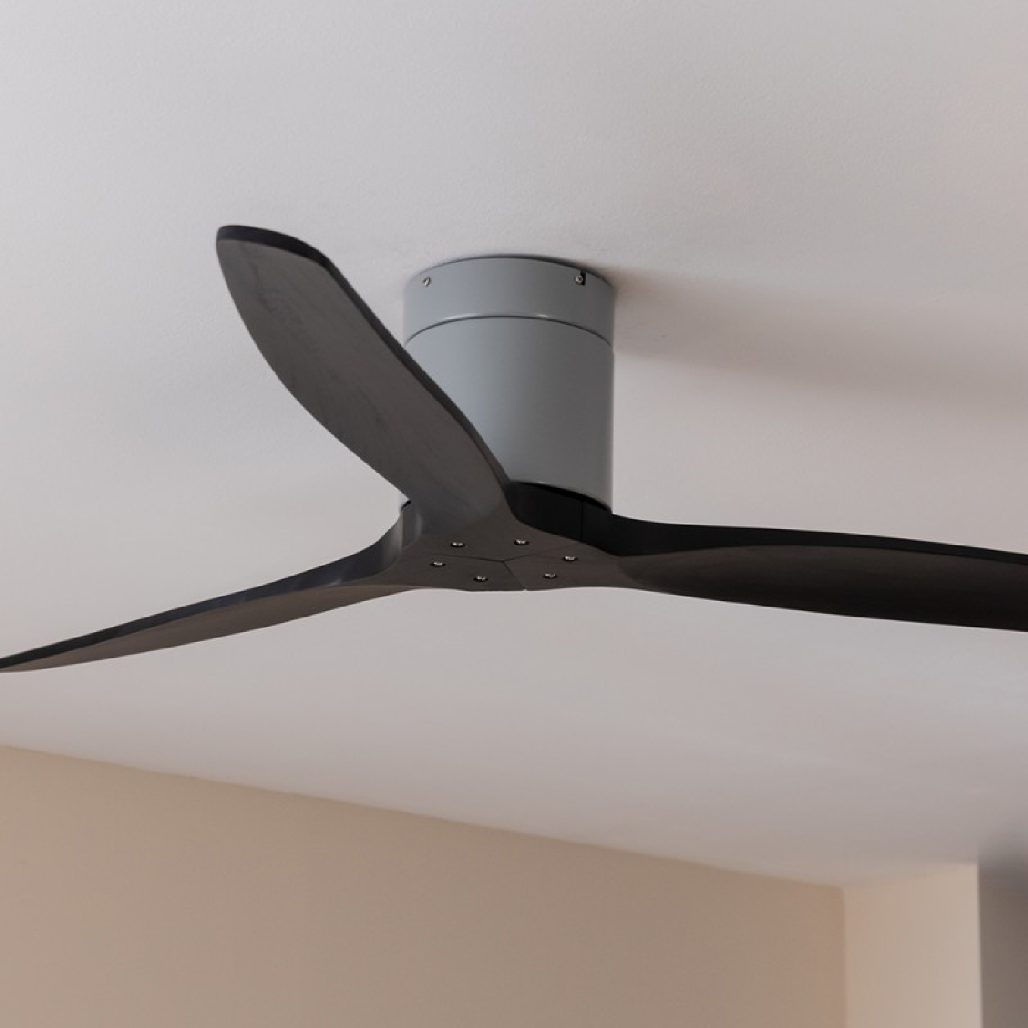Deckenventilator mit drei schwarzen Flügeln, grauem Motorgehäuse und weißer Decke.