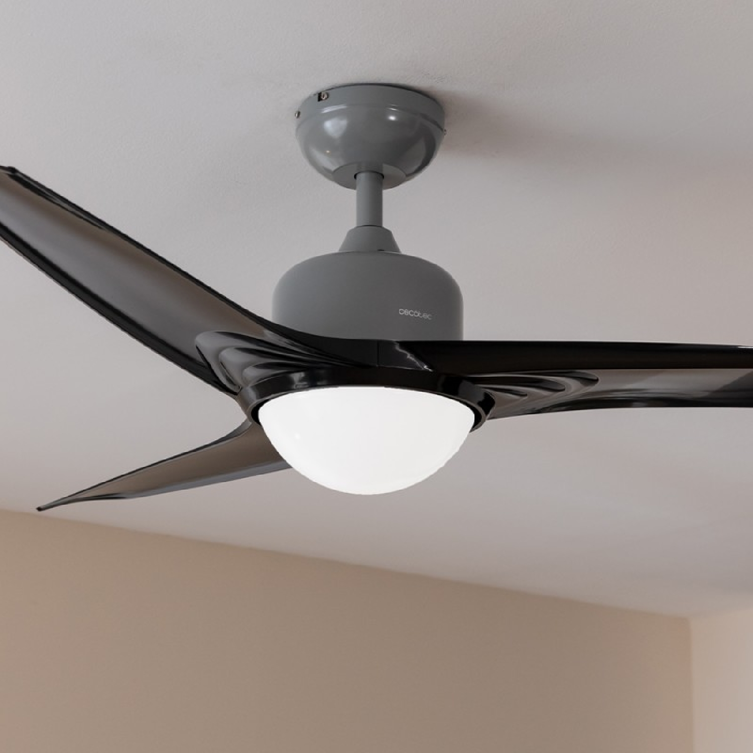 Un ventilador de techo con aspas negras y un motor gris. La luz está encendida.