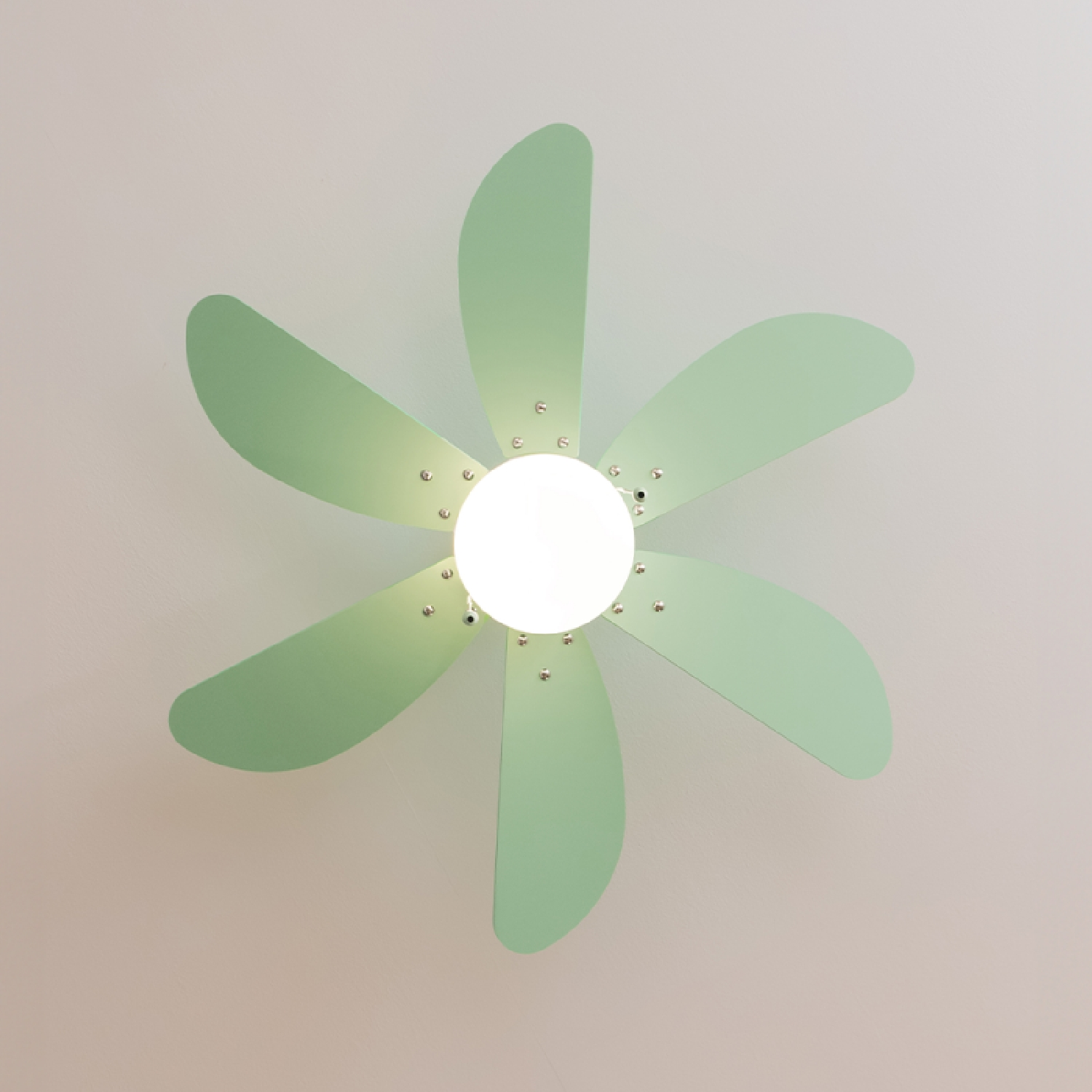 Ventilatore a soffitto con sei pale verdi e una luce centrale. Soffitto bianco e sfondo beige.