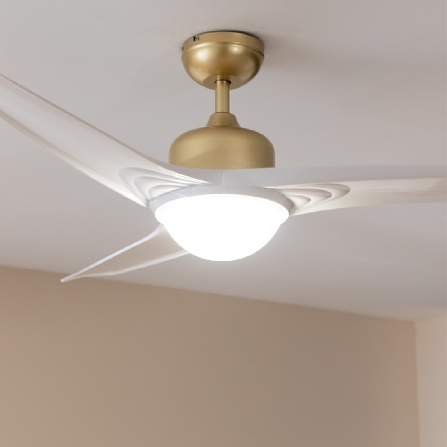 Un ventilador de techo con aspas blancas y un motor dorado. La luz está encendida.