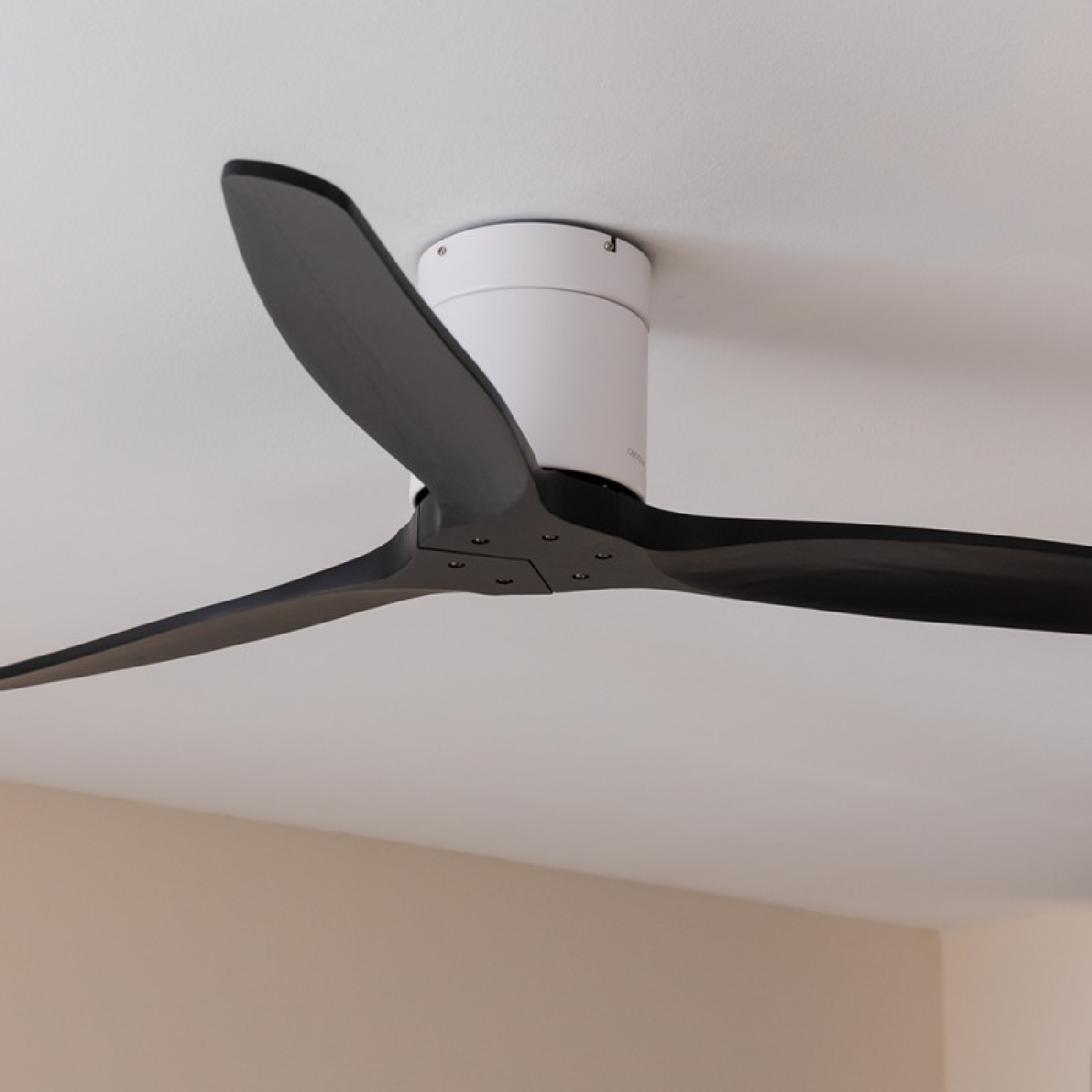 Ventilatore da soffitto con pale nere, base bianca e sfondo chiaro.