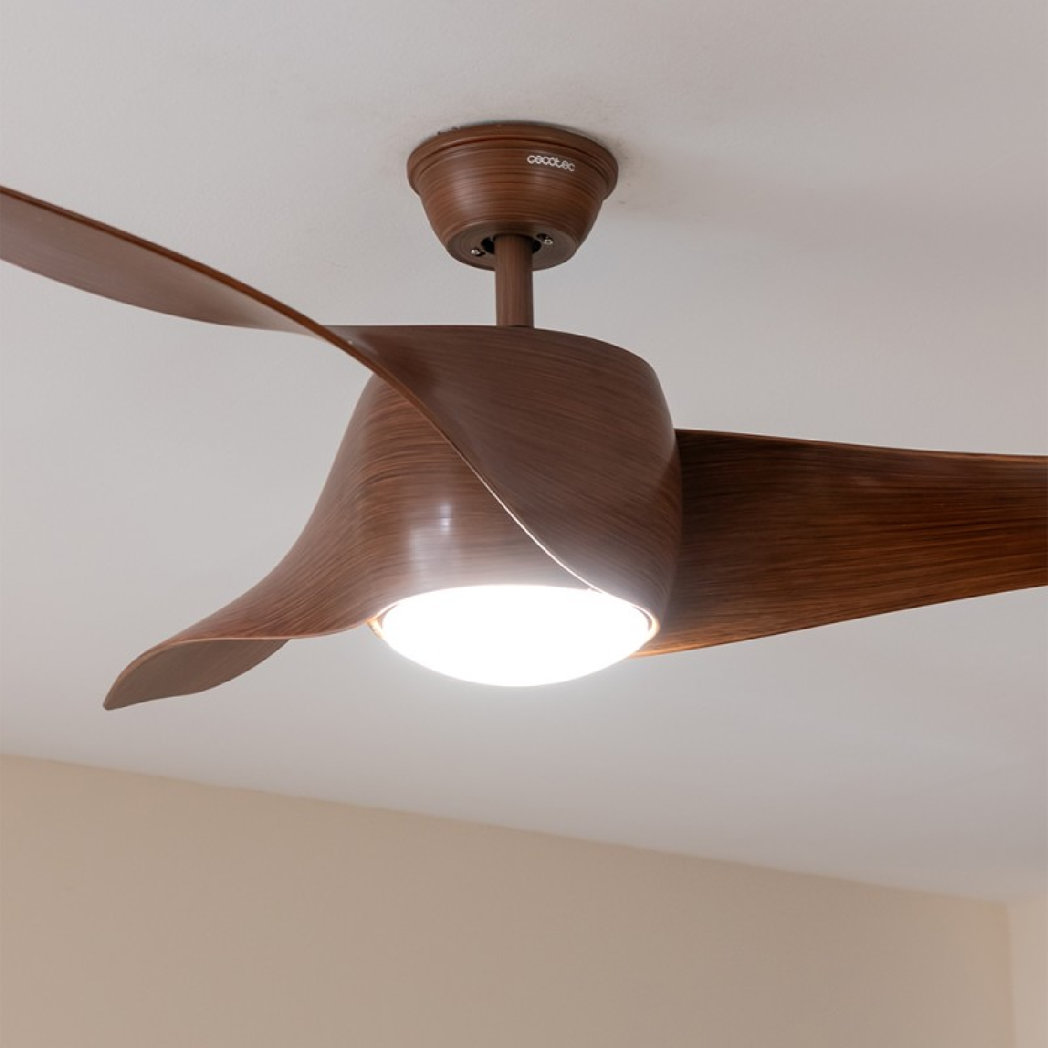 Ventilador de techo con aspas de madera, luz. Techo blanco, pared beige claro.