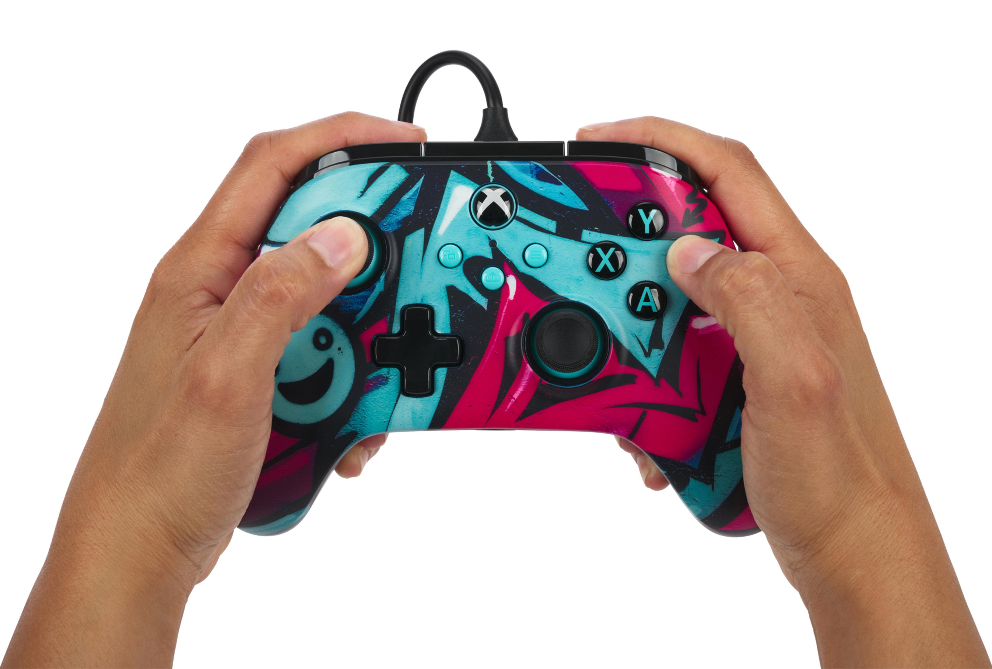 Hände halten einen Controller im Graffiti-Stil mit farbigen Knöpfen zum Spielen.