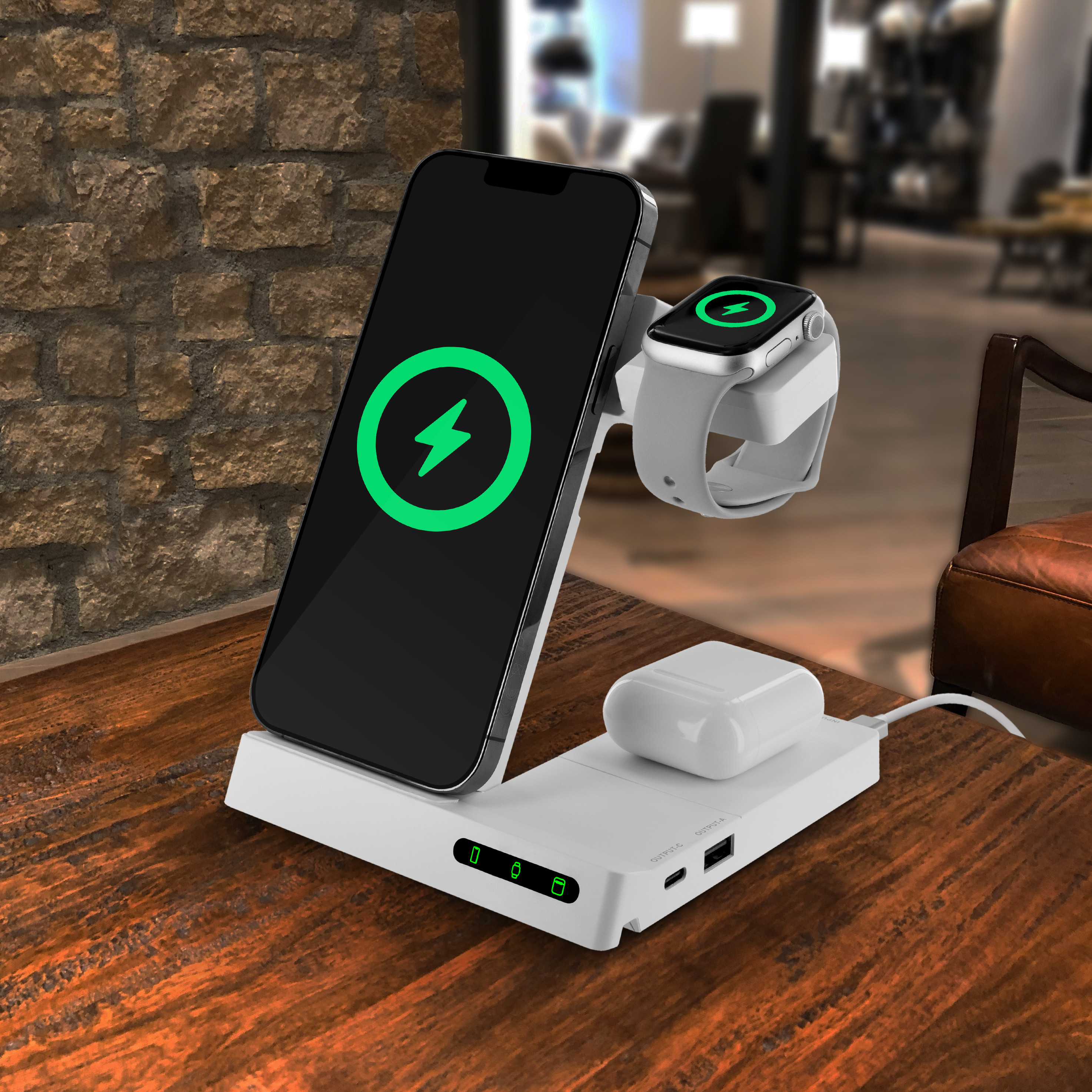 Estación de carga blanca con iPhone, Apple Watch y AirPods. Mesa de madera, fondo borroso.