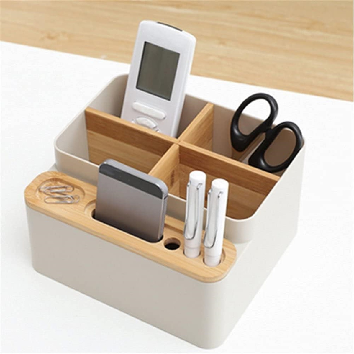 Schreibtisch-Organizer mit Fernbedienung, Stiften, Schere und Telefon in Fächern.