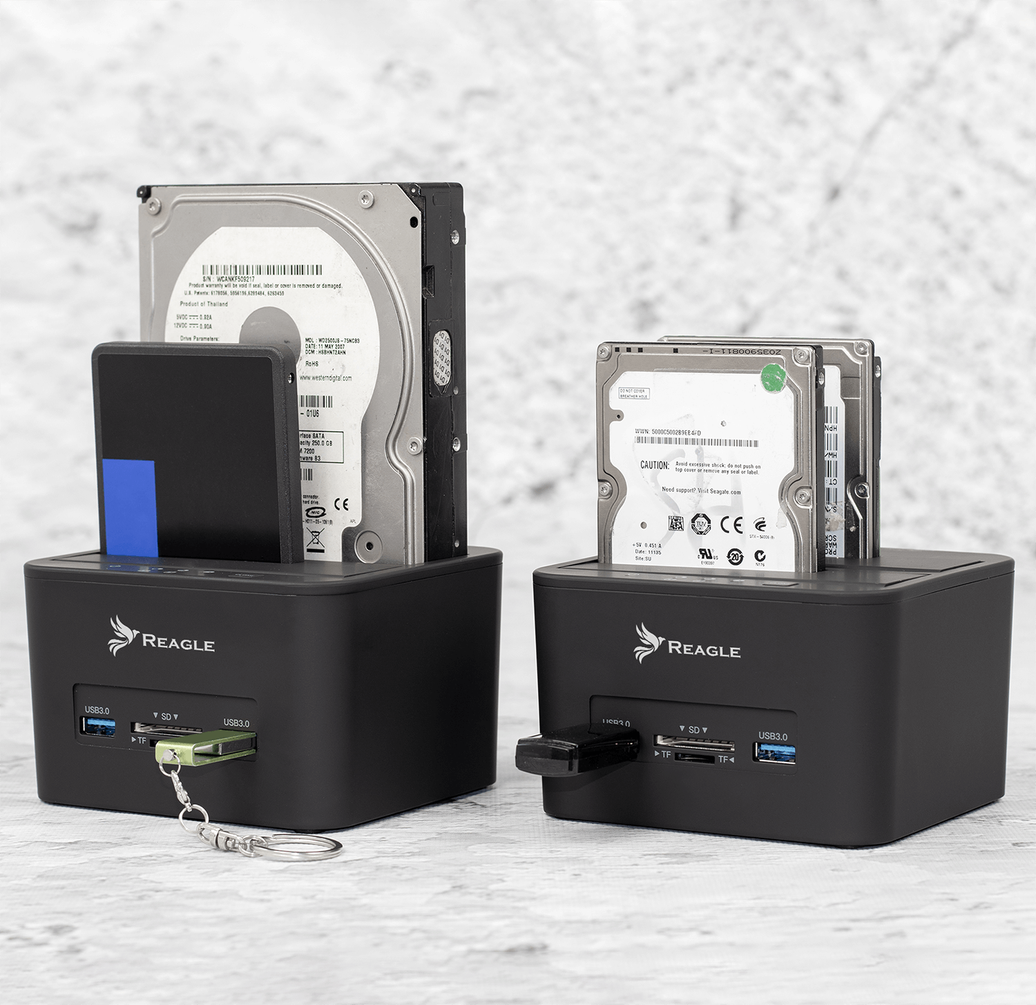 Dwie czarne stacje dokujące z dyskami twardymi i pendrivem. Jedna ma niebieski element i brelok.