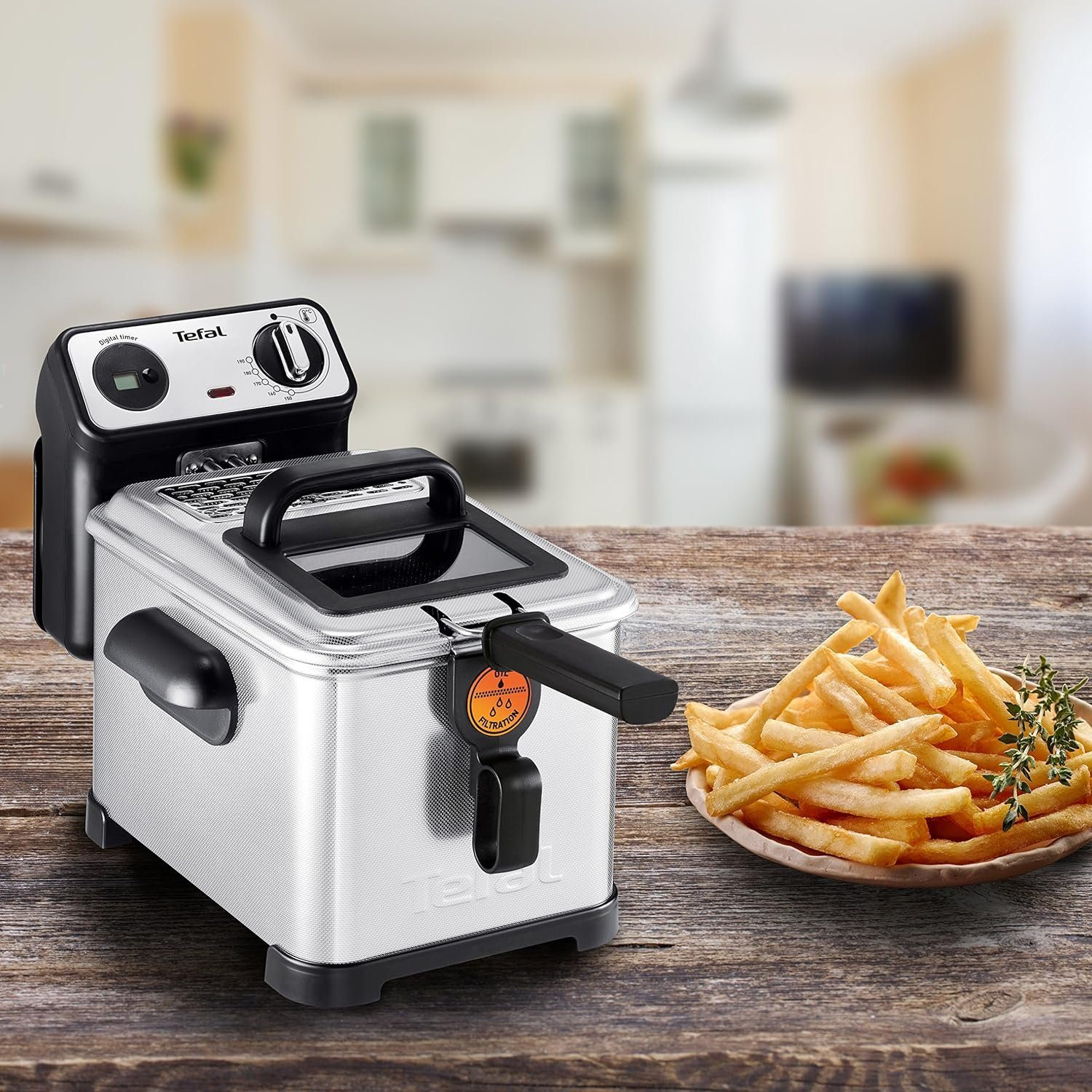 Una freidora de acero inoxidable con papas fritas en un plato. La freidora está en una mesa de madera.