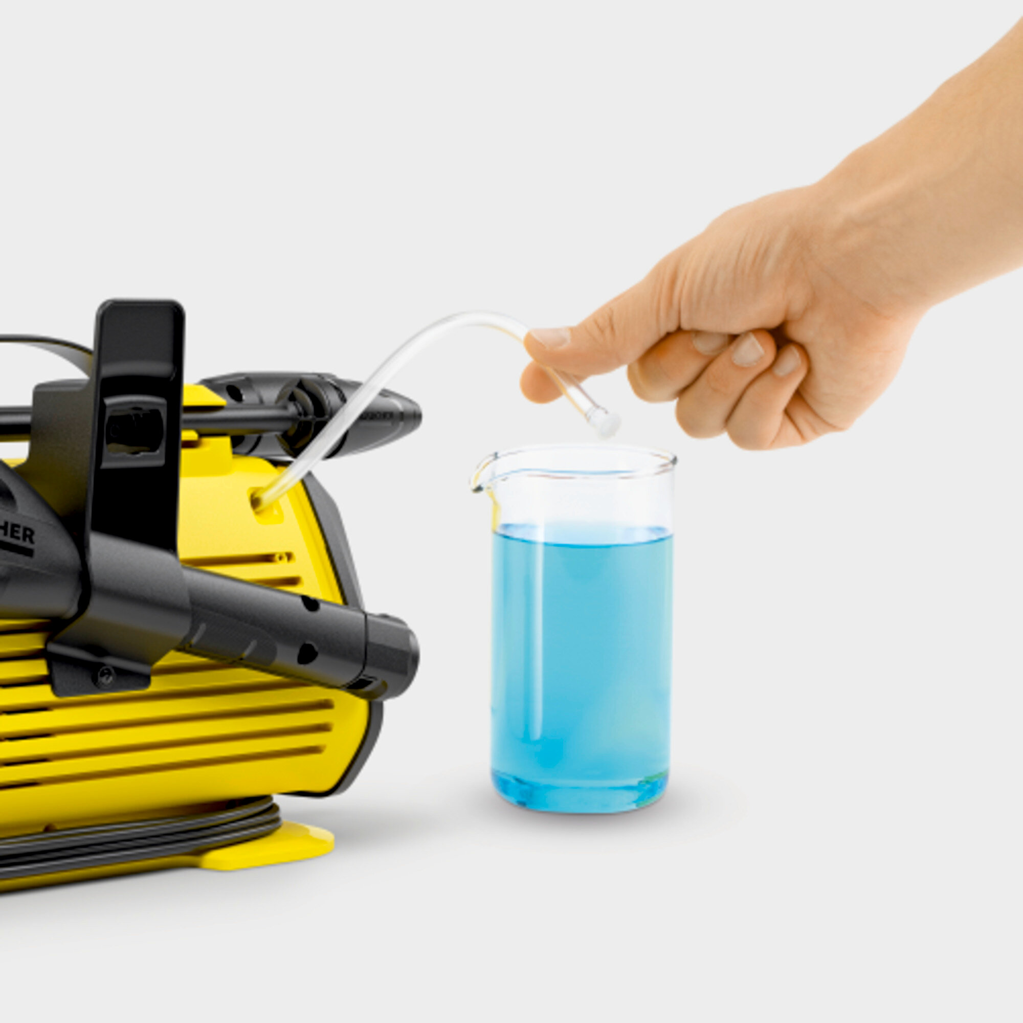 Een hand giet blauwe vloeistof in een beker uit een transparante slang. Naast een gele machine.