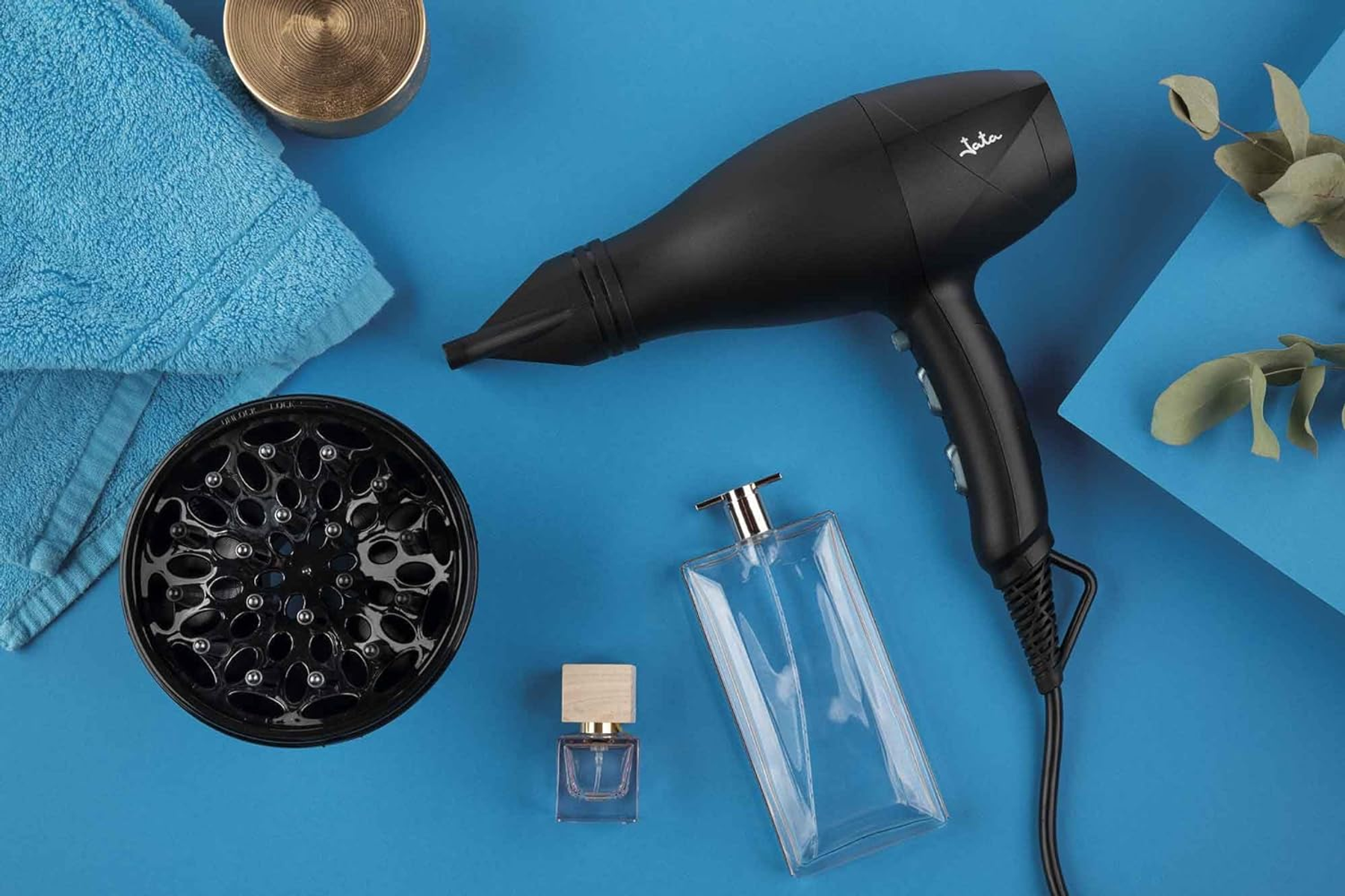 Czarna suszarka do włosów, dyfuzor, butelki perfum i niebieski ręcznik na niebieskiej powierzchni.