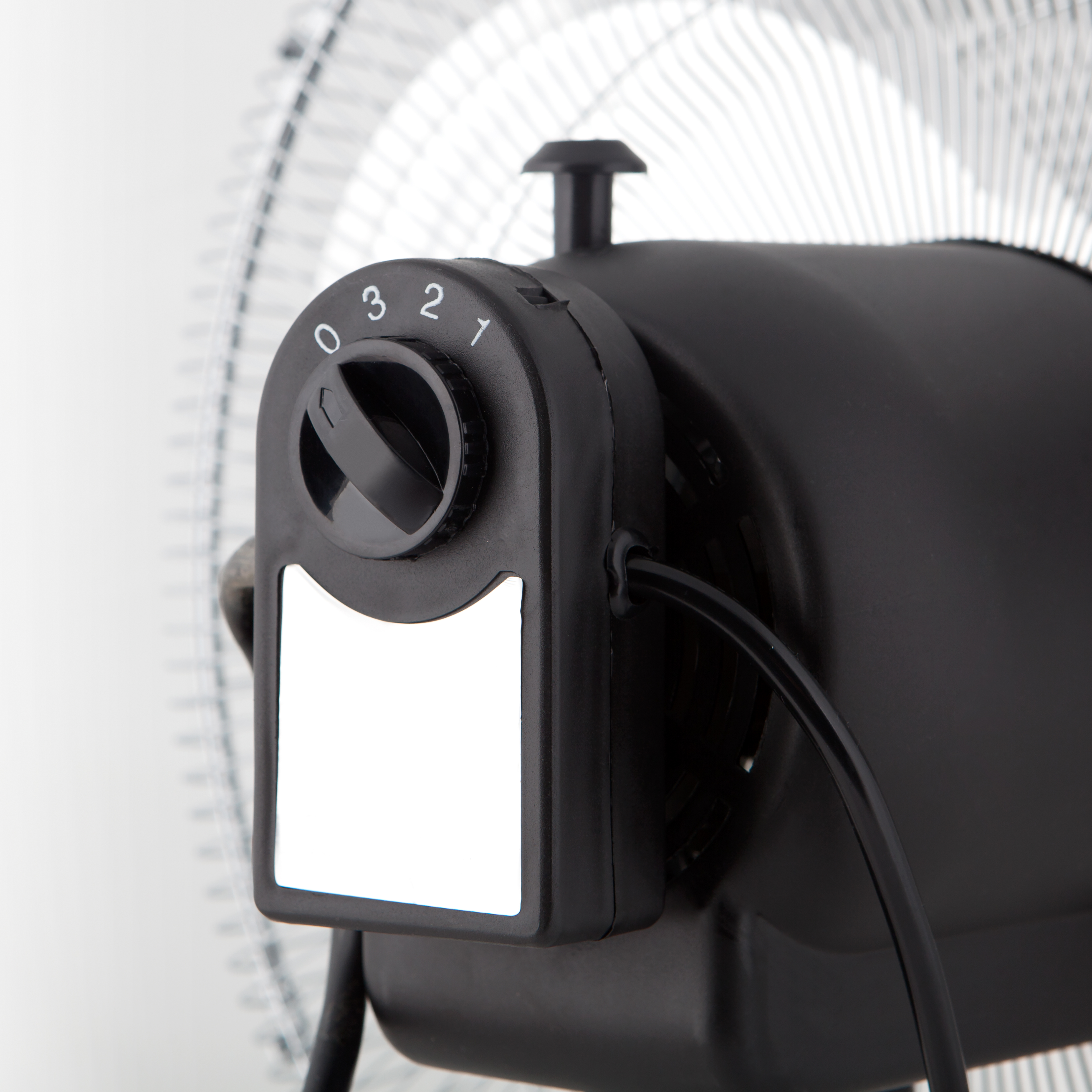 Primer plano de un panel de control de ventilador negro con números, un dial y una etiqueta blanca en blanco.