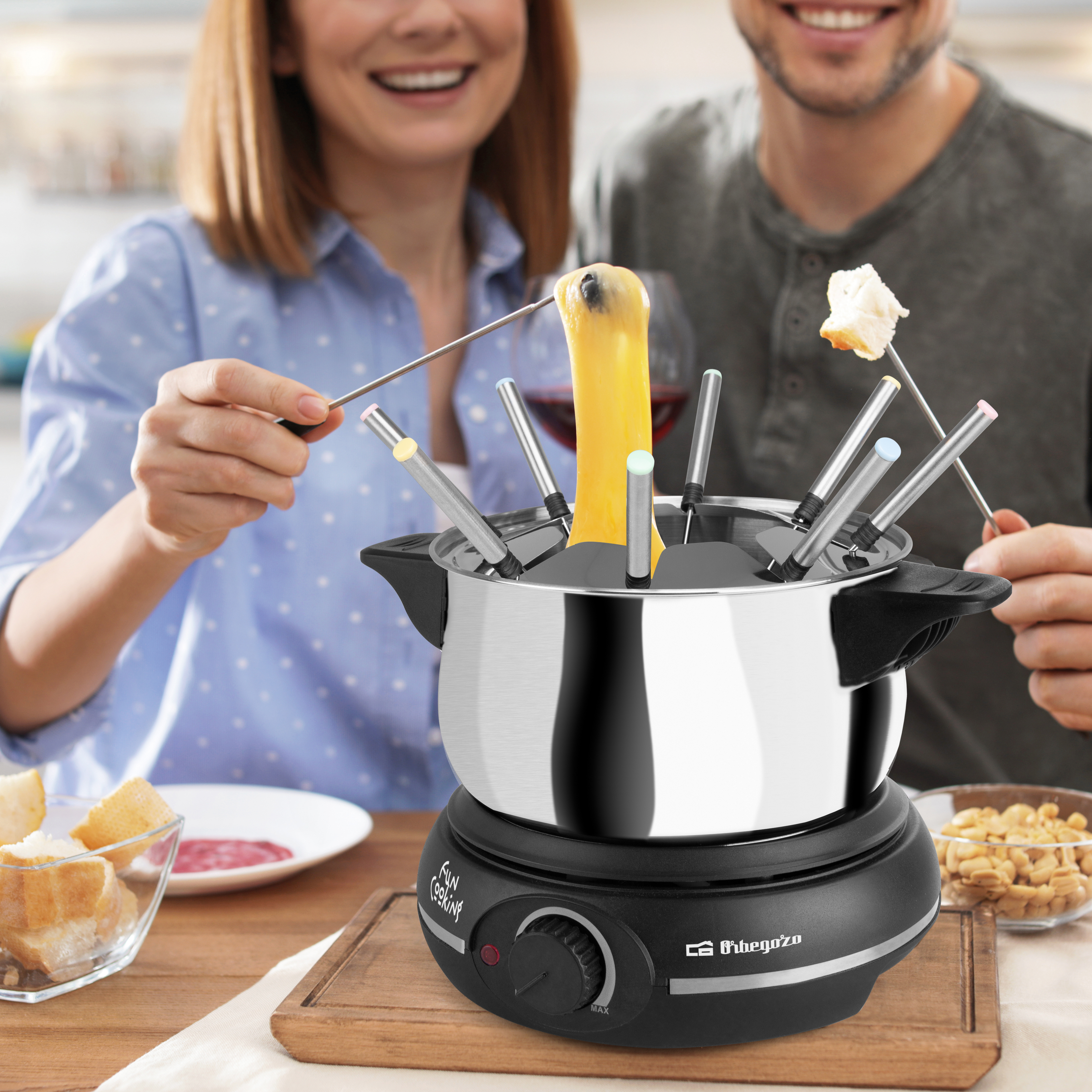 Ludzie zanurzający jedzenie w garnku do fondue z szaszłykami i drewnianą tacą z przekąskami.