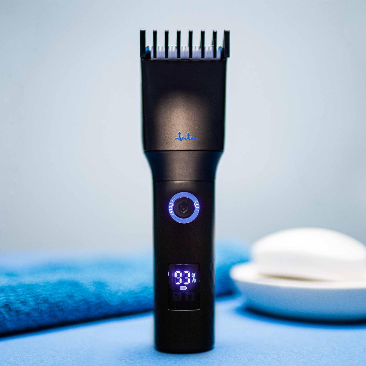 Cortadora de cabello negra con pantalla digital y detalles azules sobre superficie azul.