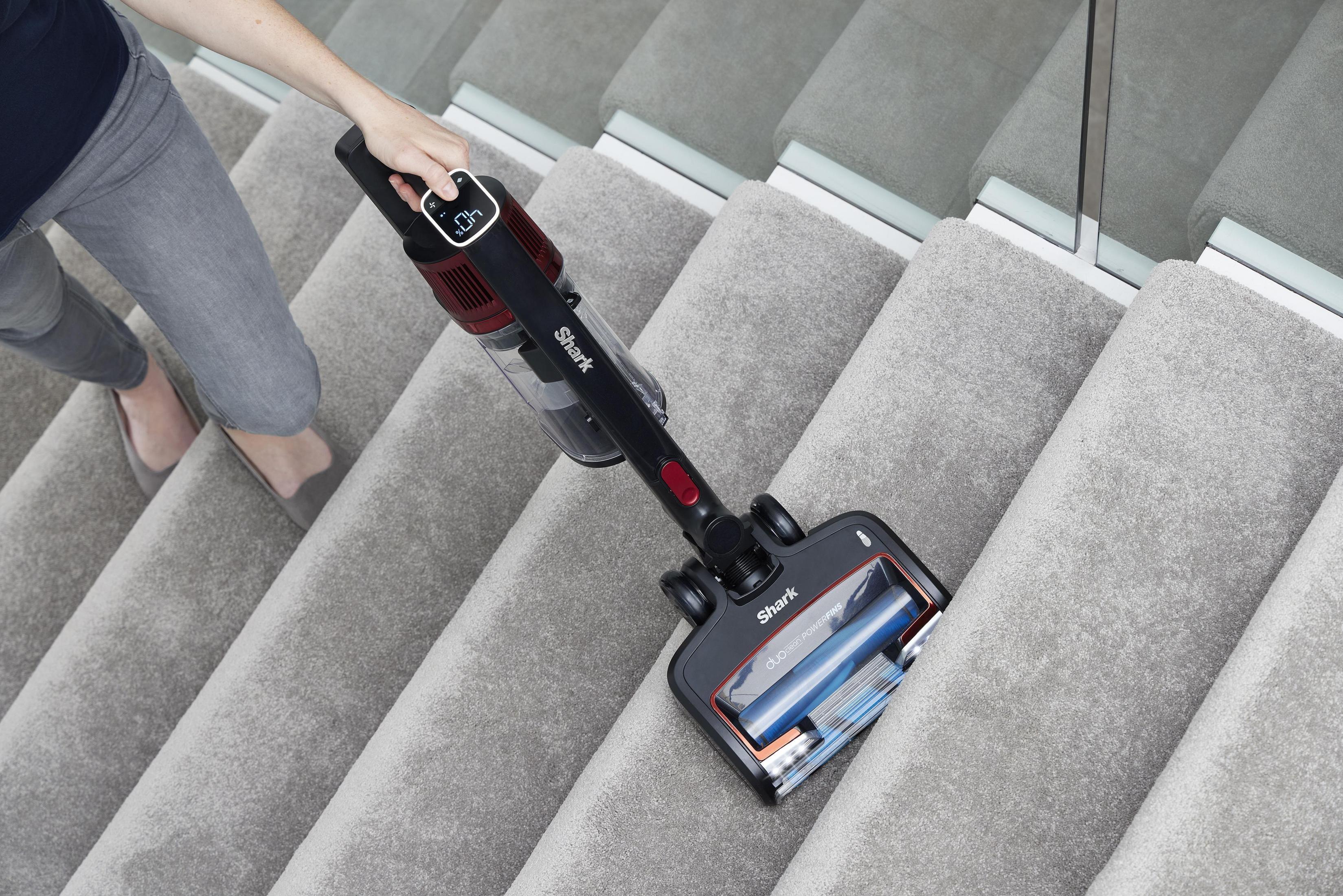 Eine Frau saugt eine Teppichtreppe mit einem kabellosen, handgehaltenen Staubsauger.