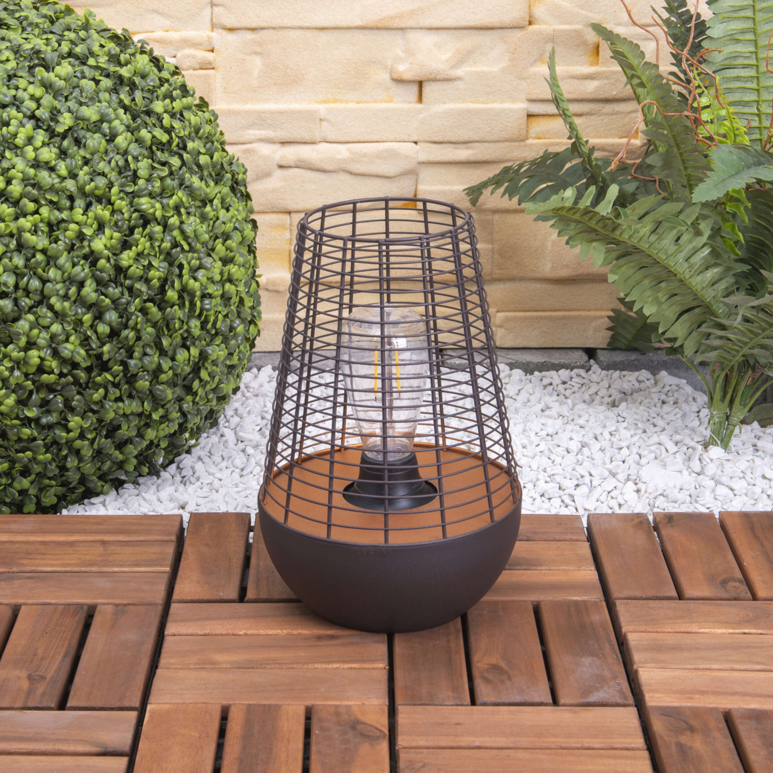Eine schwarze Metall-Außenlampe mit einer Glühbirne. Sie steht auf einem Holzdeck mit Steinhintergrund.