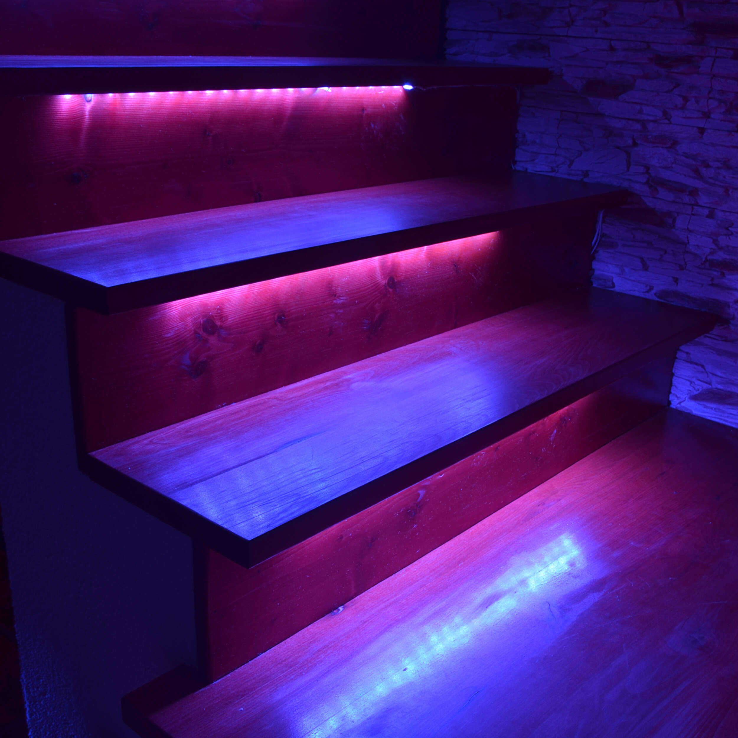 Holztreppe mit eingebauter roter und blauer LED-Beleuchtung, die die Stufen beleuchtet.