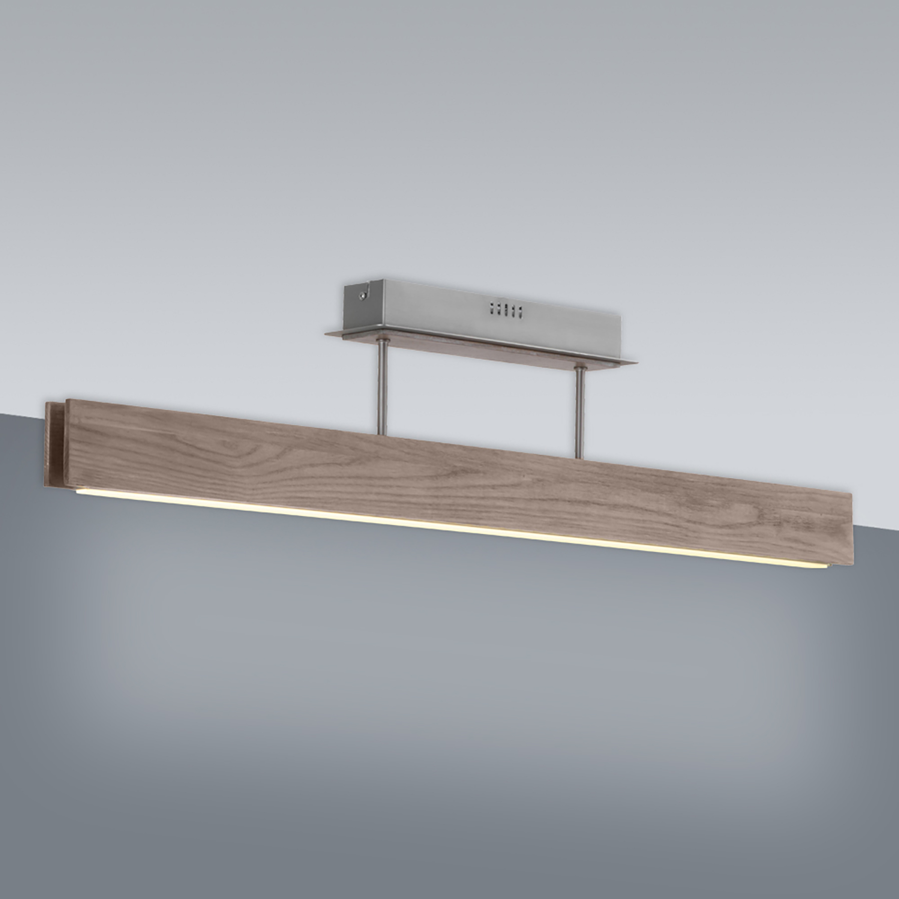Eine lange Deckenleuchte aus Holz mit Metallbasis vor einer grauen Wand.