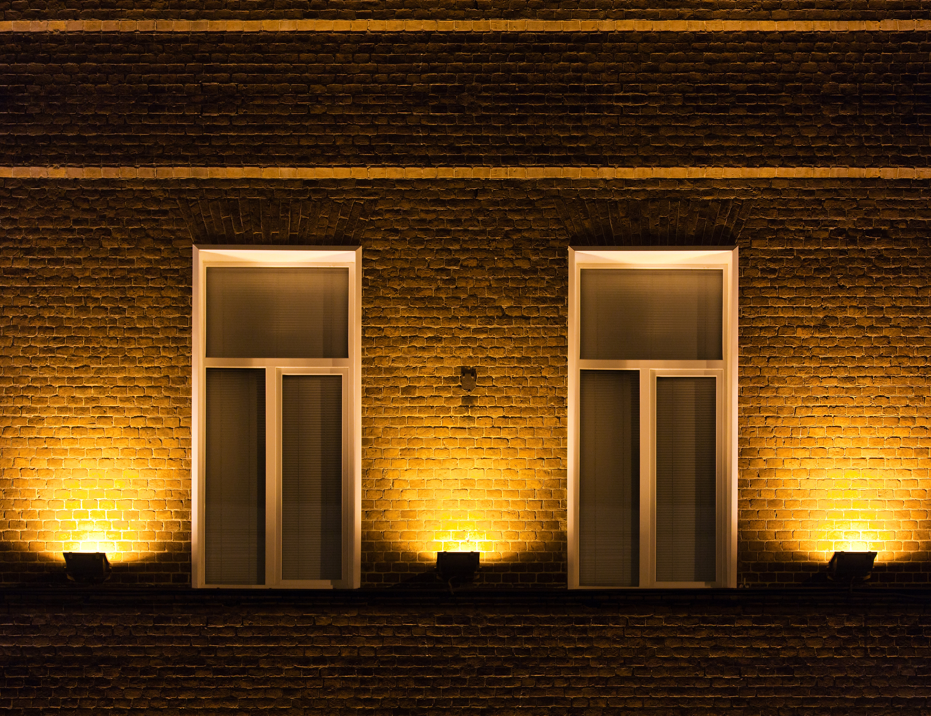 Zwei Fenster mit Lichtern, Backsteinmauer bei Nacht.