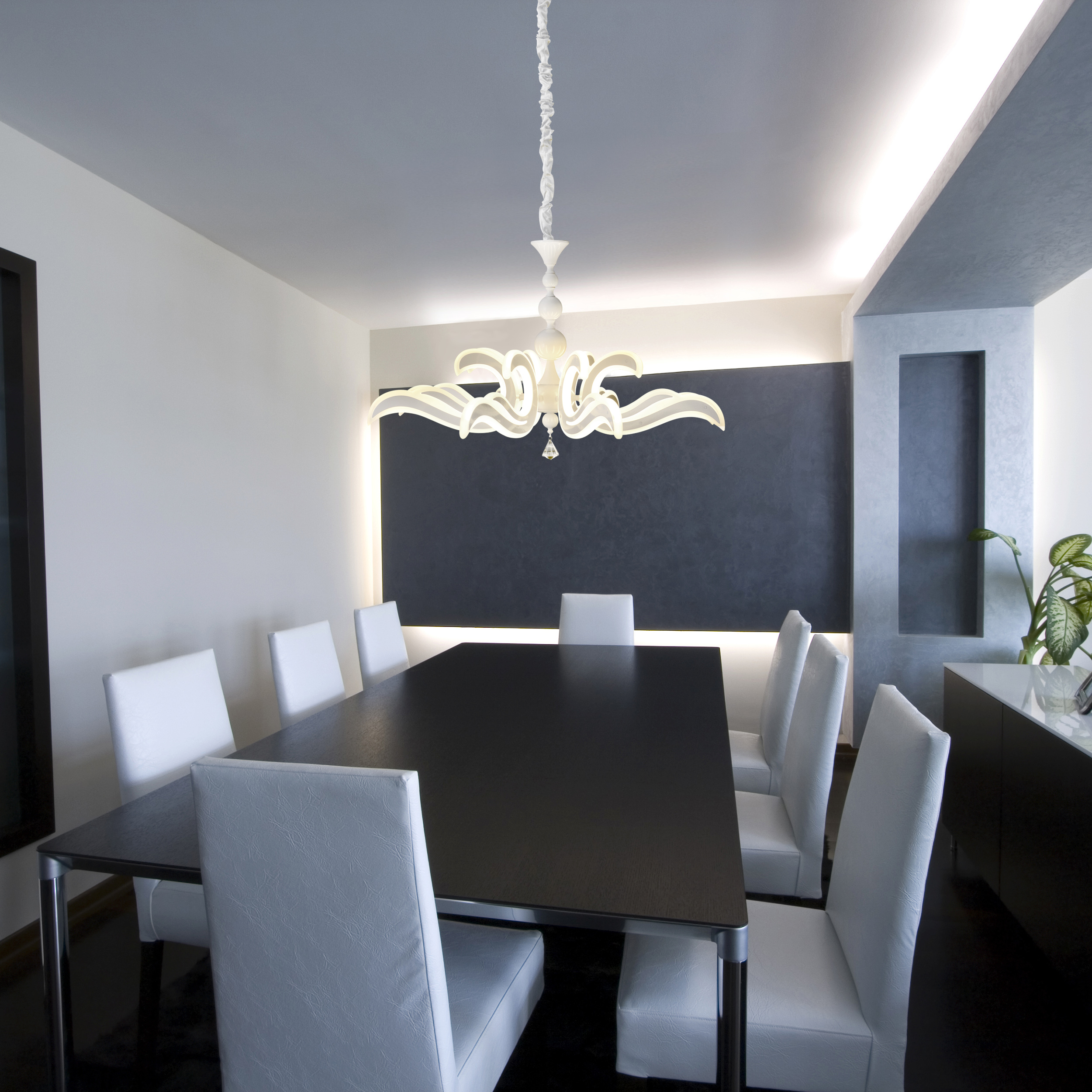 Esszimmer mit schwarzem Tisch, weißen Stühlen und Kronleuchter. Weiße Wände.