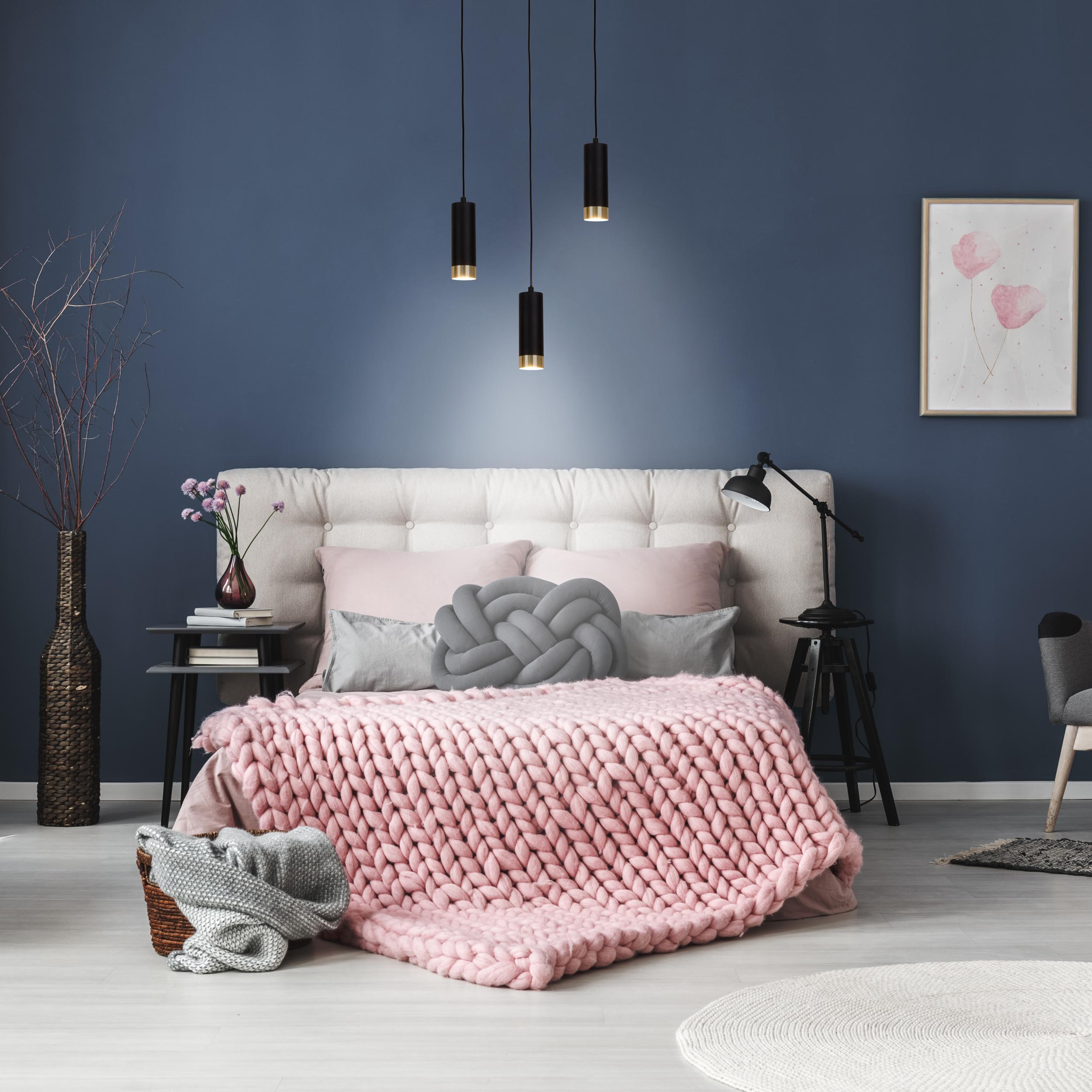 Ein Schlafzimmer mit Bett, rosa Decke und Hängelampen vor blauer Wand.