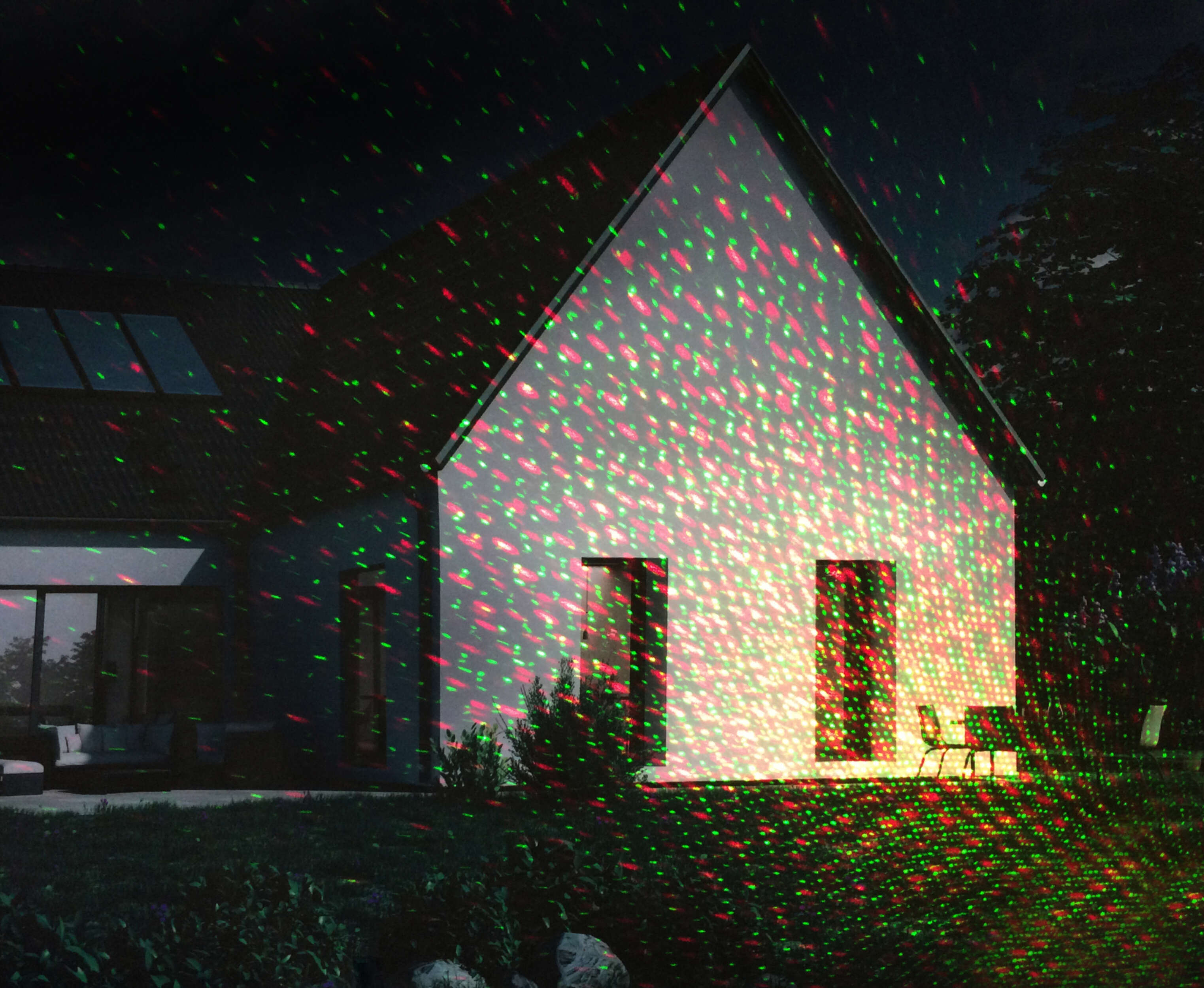 Haus bei Nacht mit roten und grünen Laserlichtern auf der Fassade. Grünes Gras und dunkler Himmel.