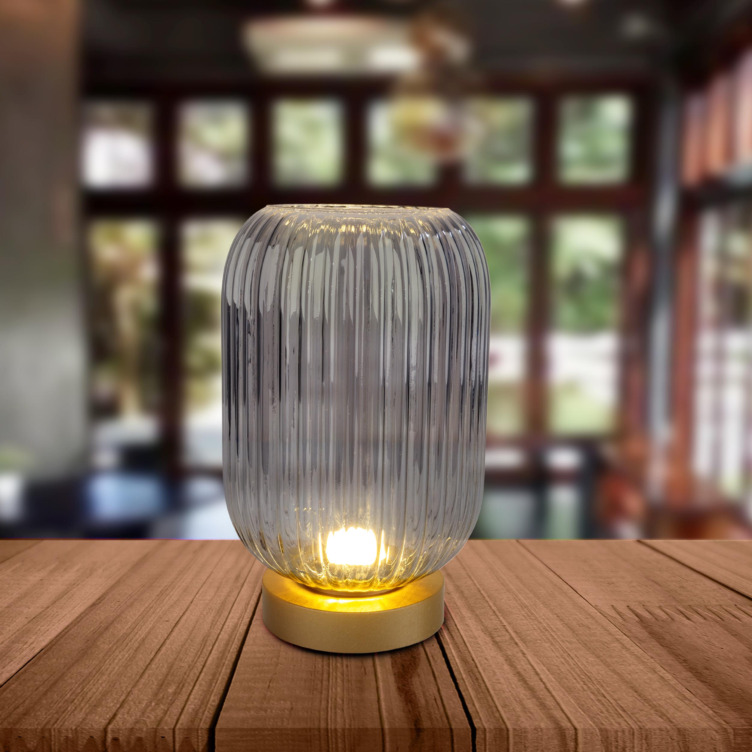 Eine Glaslampe mit goldenem Fuß auf einem Holztisch. Verschwommener Hintergrund.