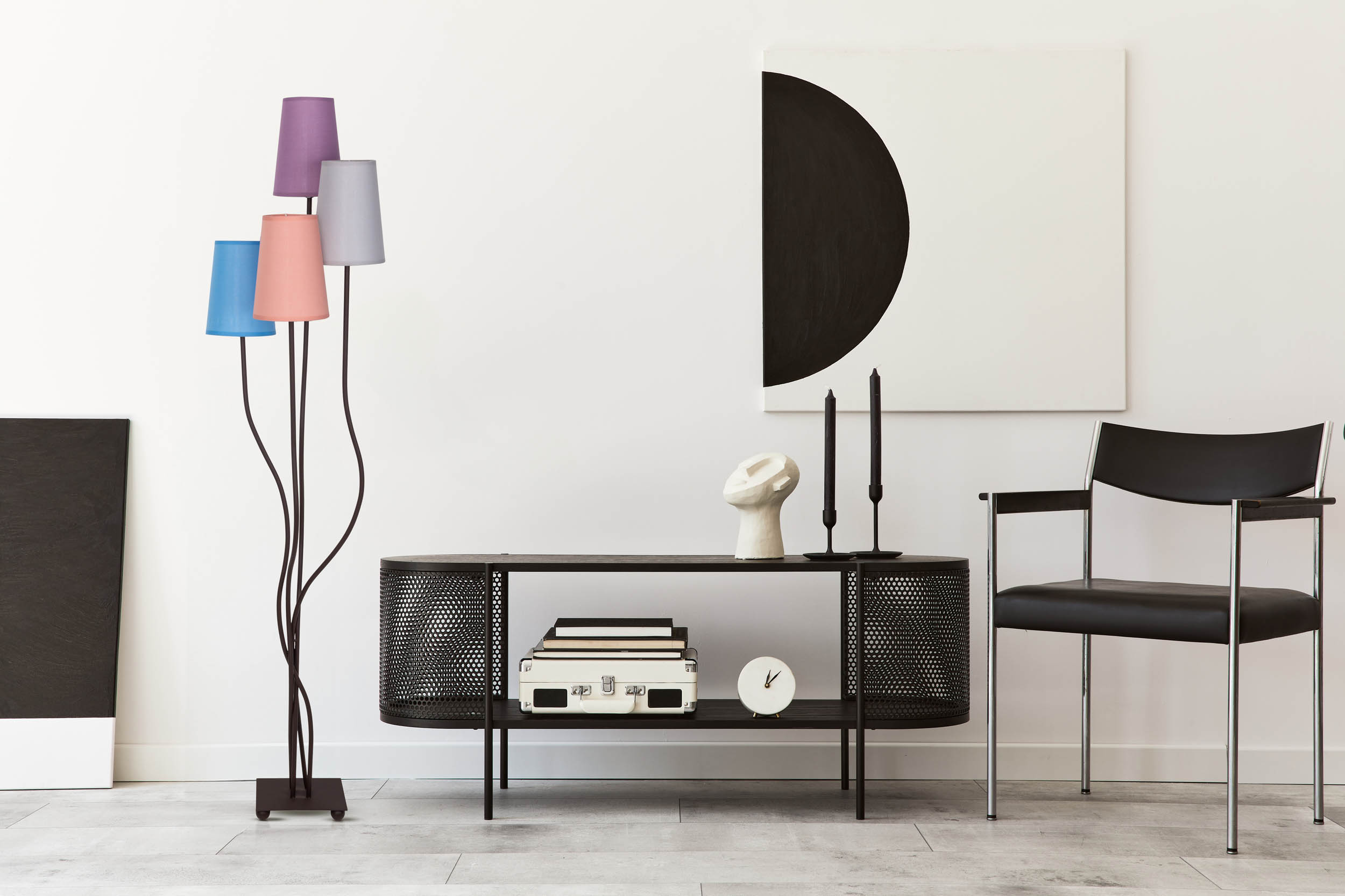 Stehlampe mit bunten Schirmen. Eine schwarze Konsole mit Deko und ein schwarzer Stuhl.