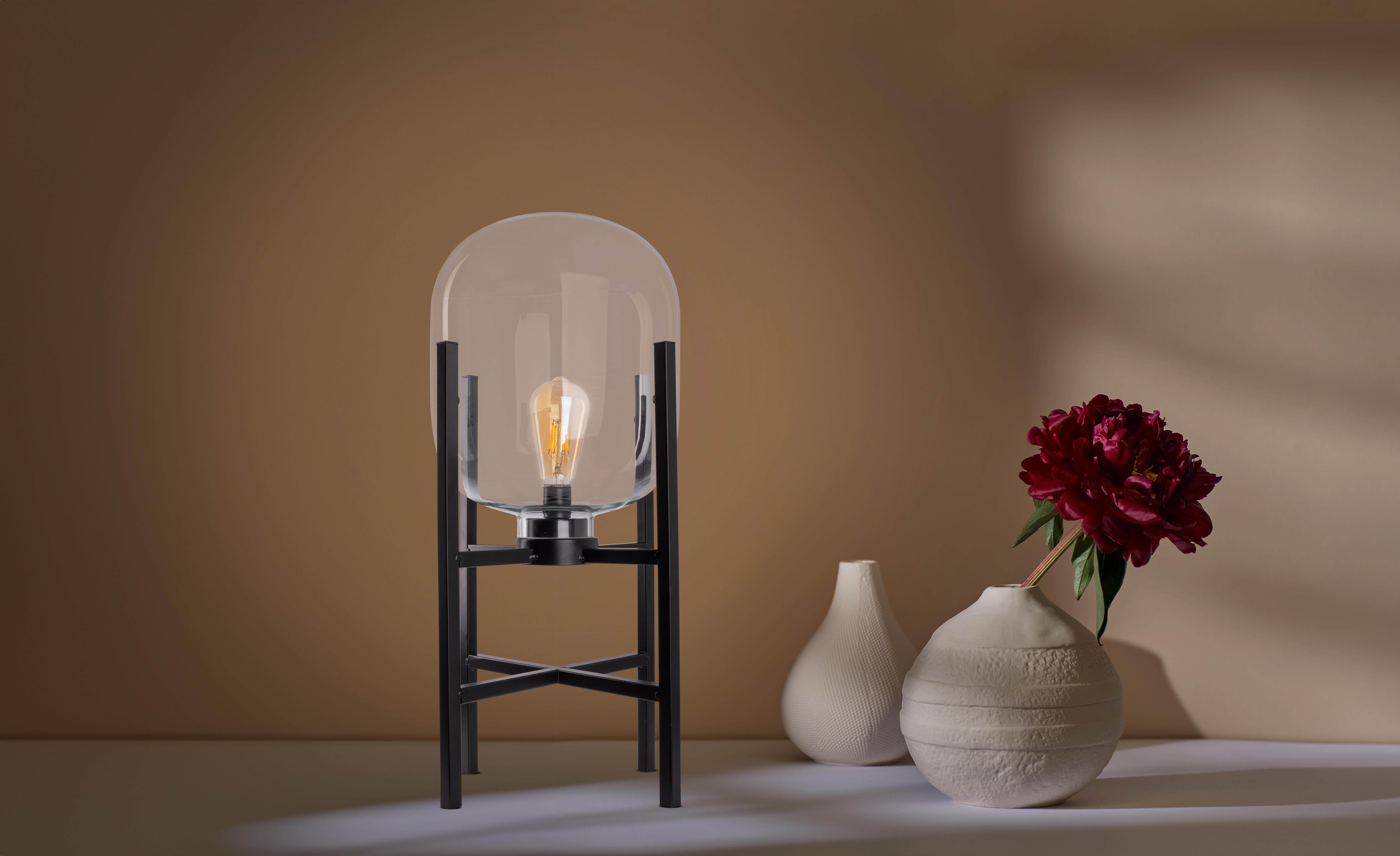 Tischlampe mit großem Glasschirm. Lampe steht auf einem schwarzen Ständer mit Blume und Vase.