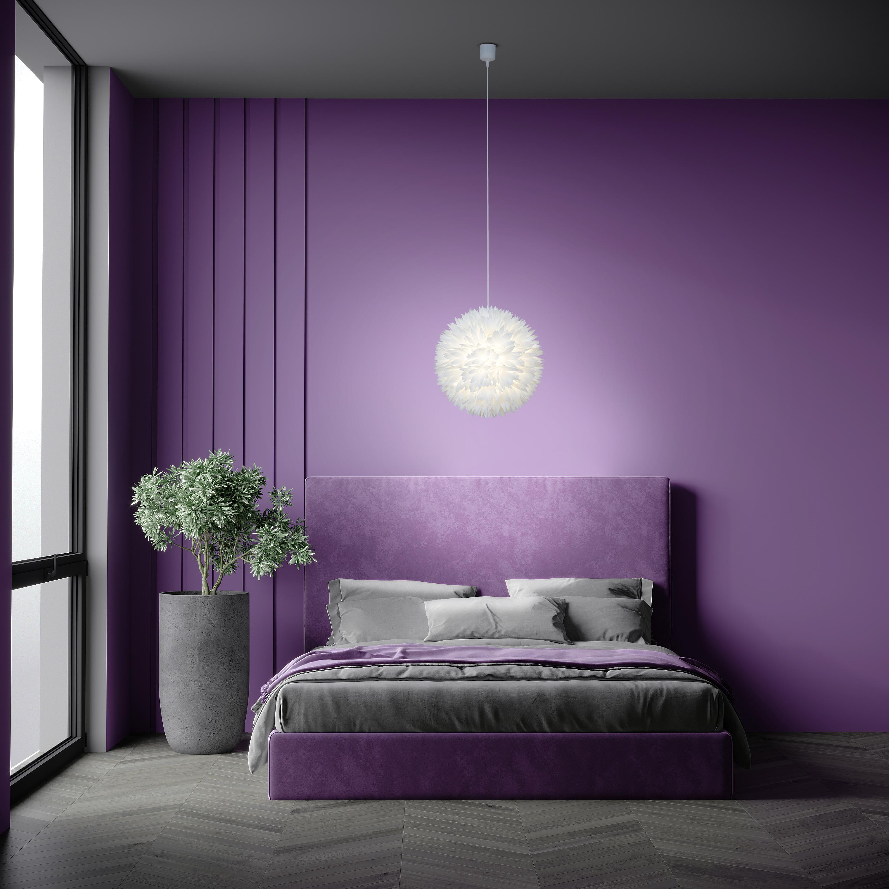 Schlafzimmer mit lila Wänden, Bett und Hängeleuchte. Eine Topfpflanze steht am Fenster.