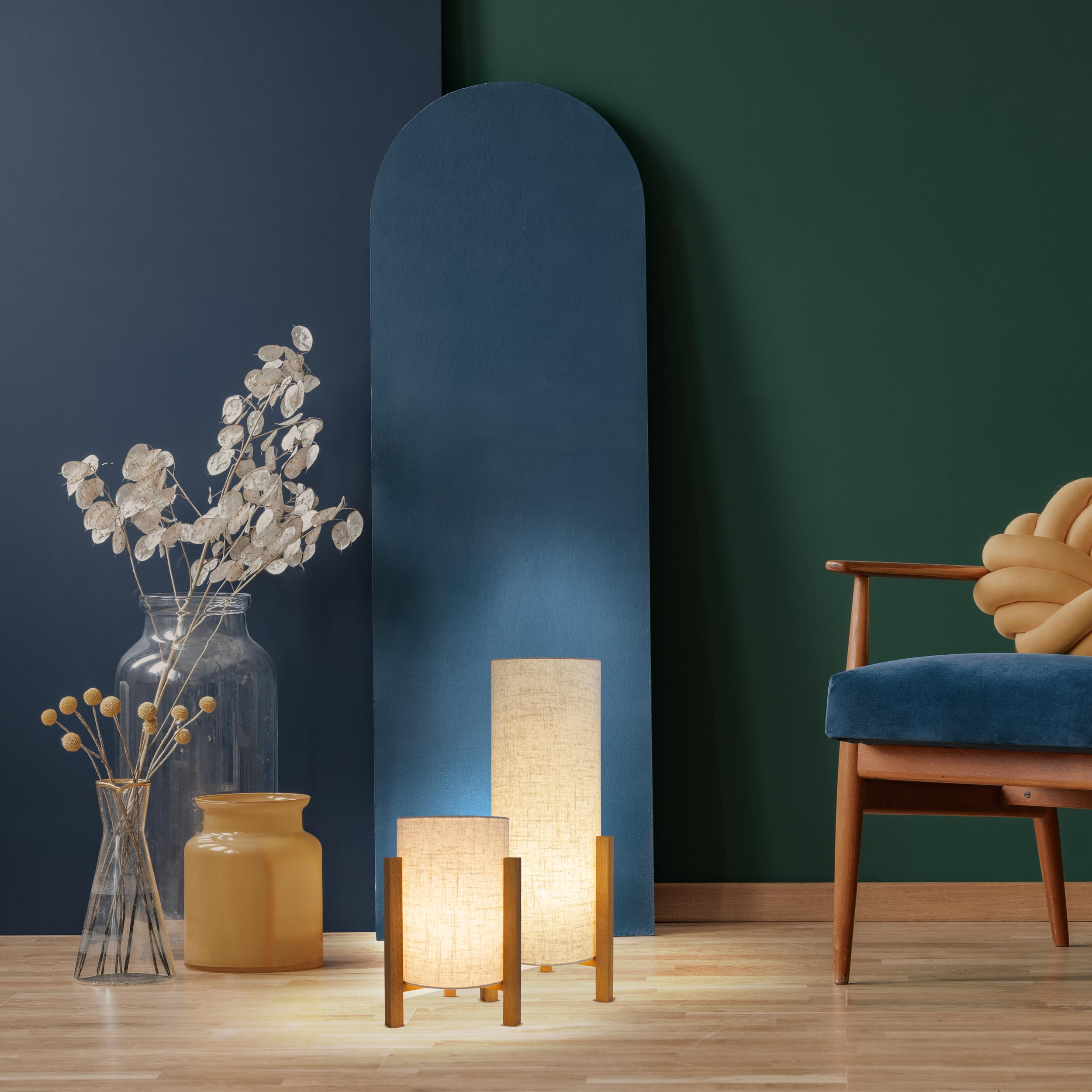 Zimmer mit Lampen, Spiegel und Stuhl. Lampen sind aus Holz, Stuhl blau. Hintergrund ist blau und grün.