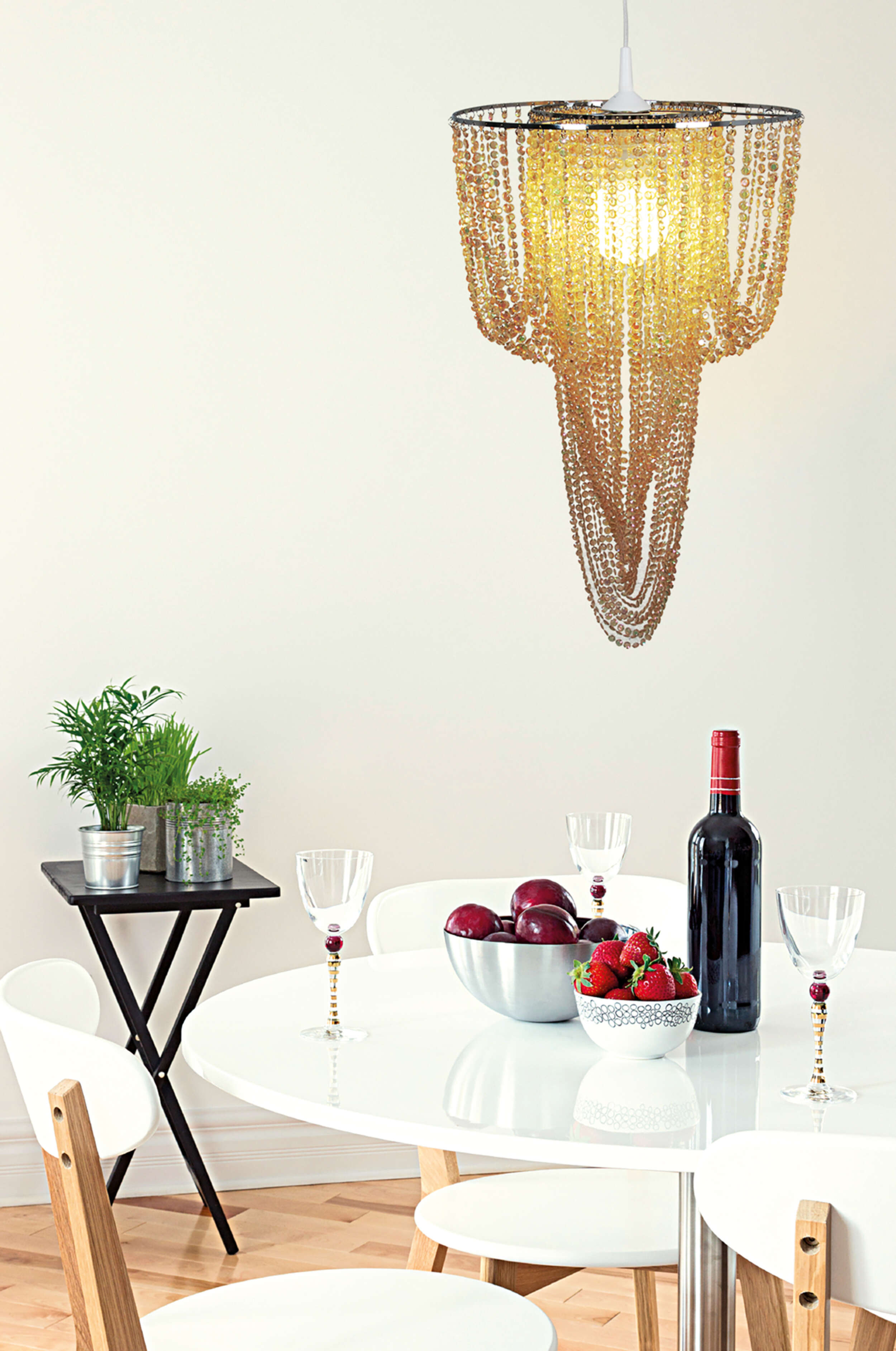 Esstisch mit Wein, Gläsern, Obst und Kronleuchter, mit weißen Wänden.
